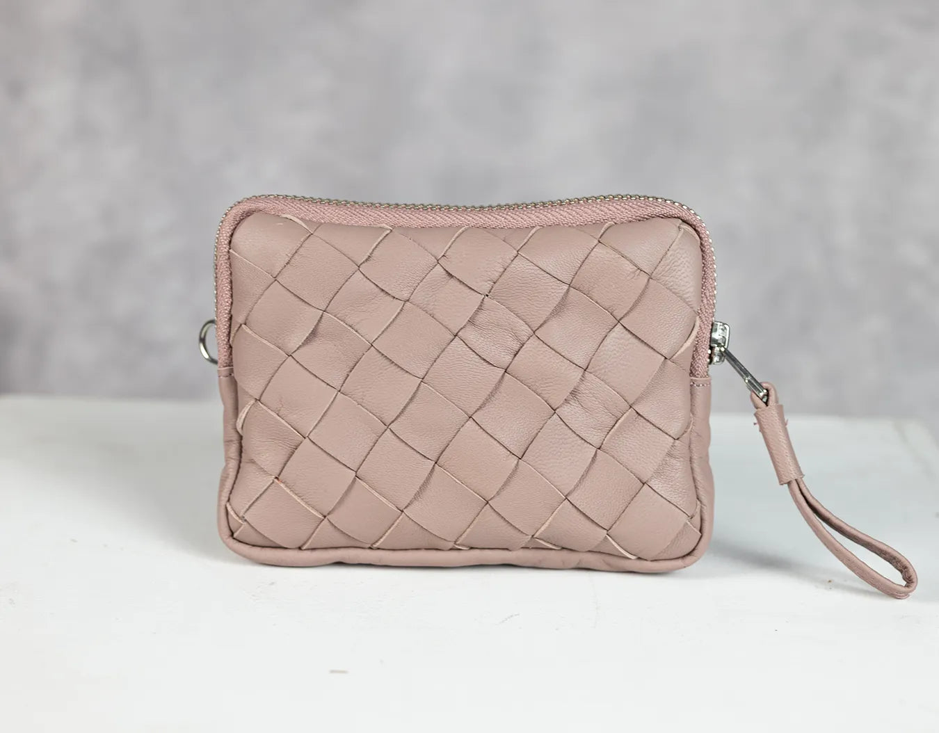 Pink woven clutch bag on a white surface with a gray background