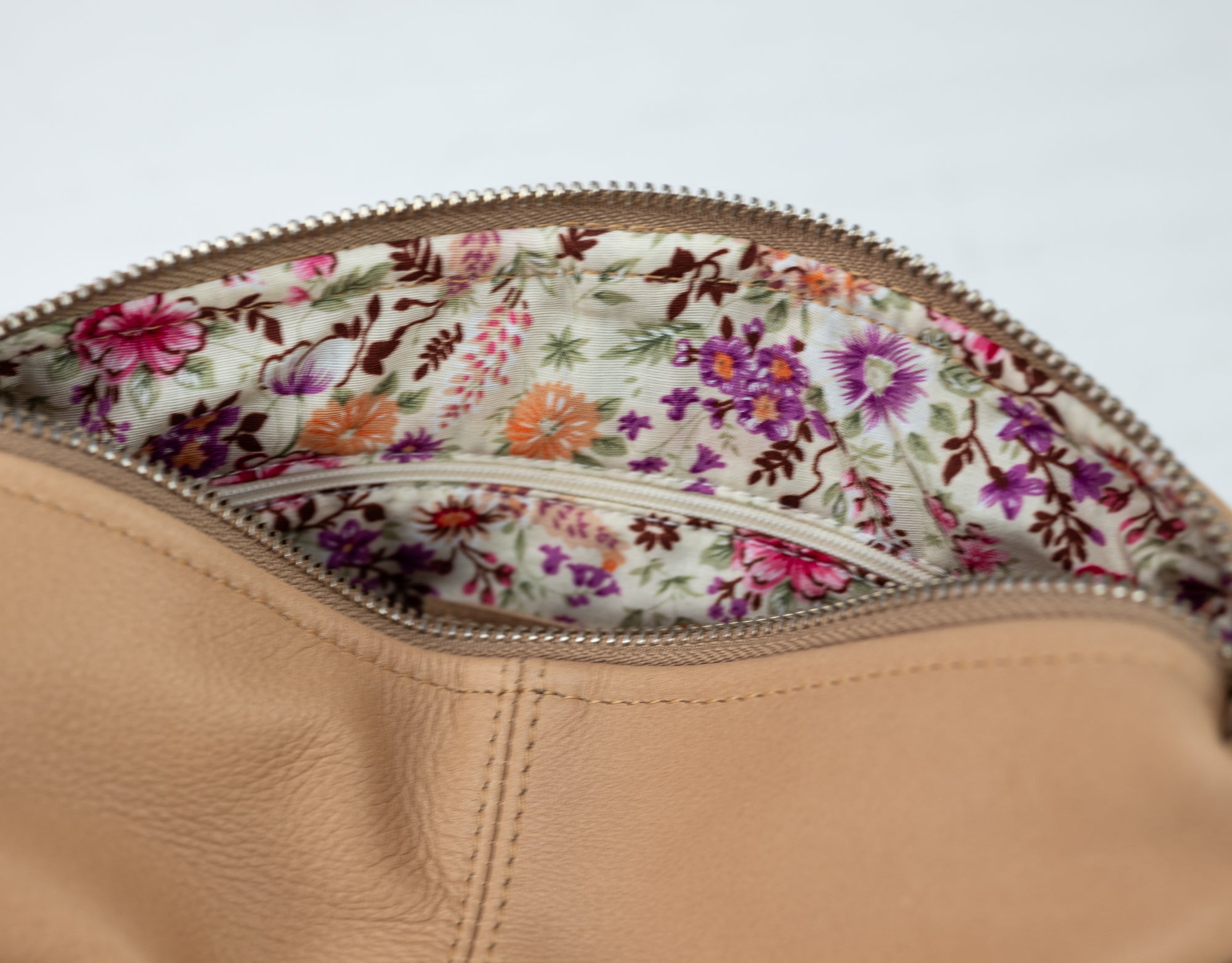 Close-up of a beige leather bag with floral lining on a light gray background