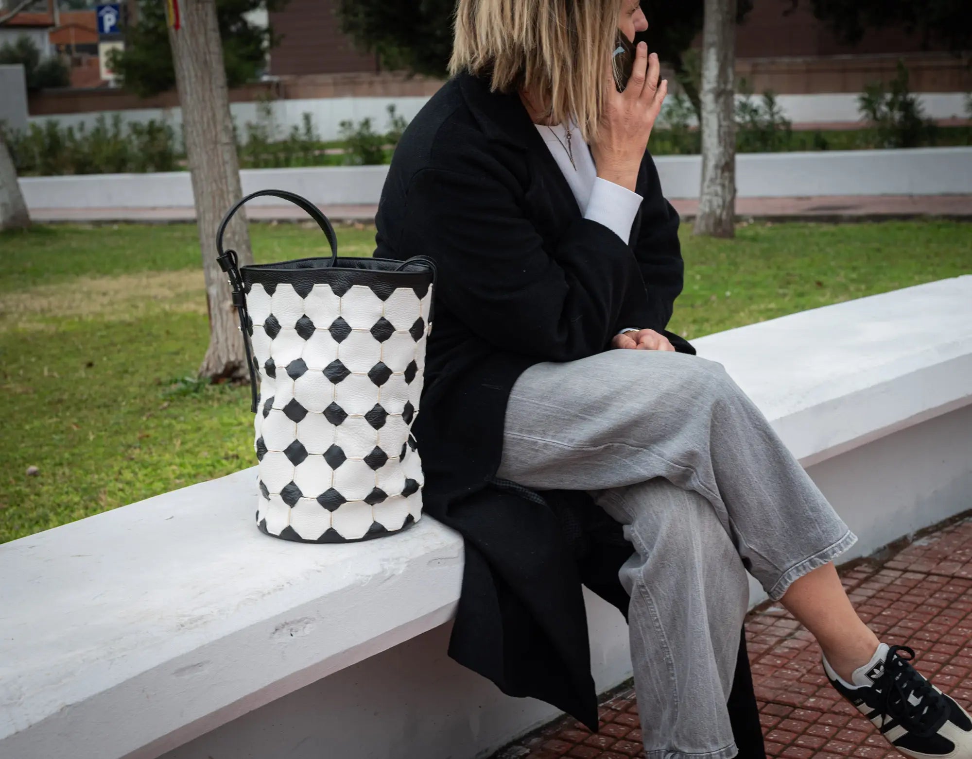 Person sitting on a bench with a patterned bag next to them, outdoors.