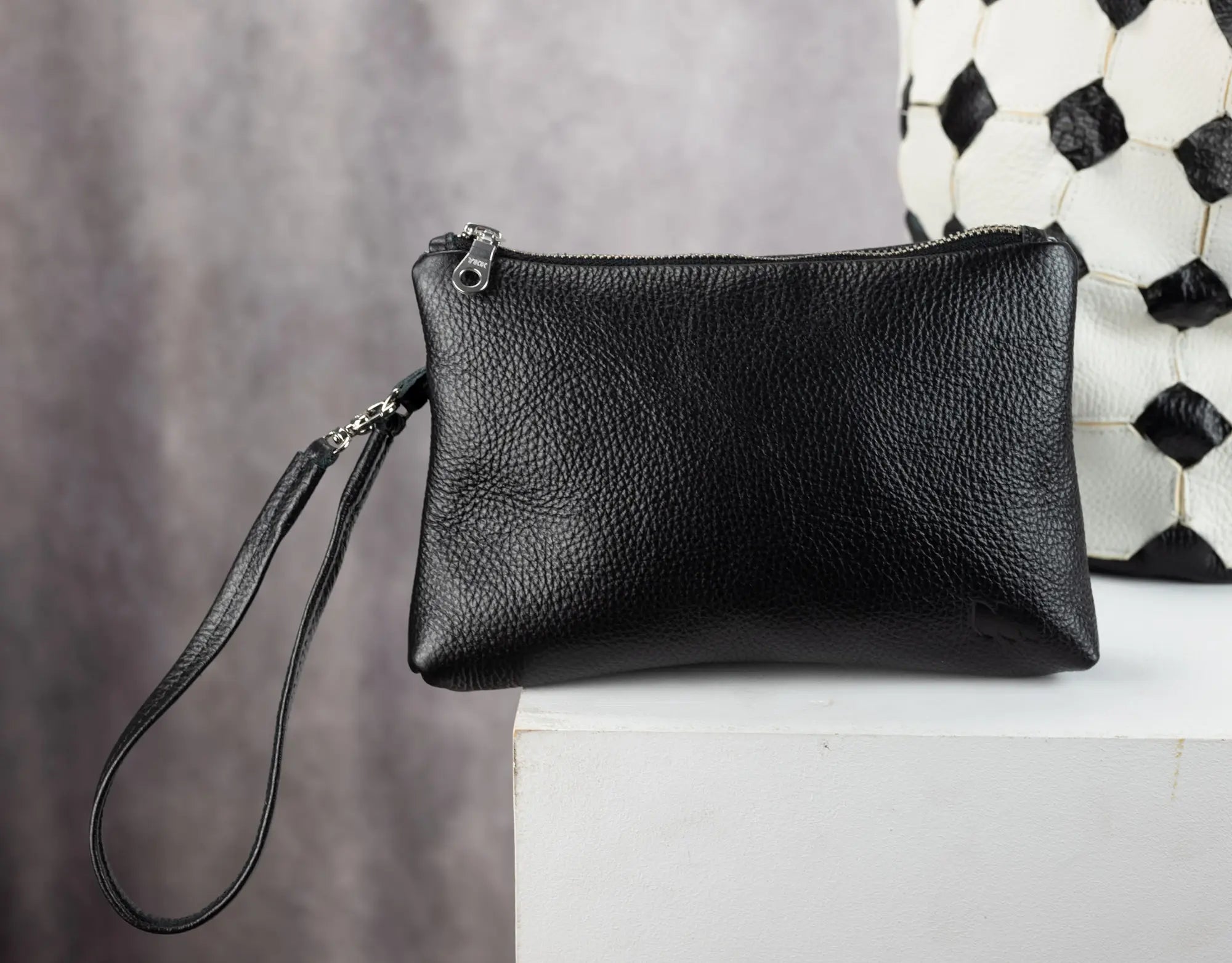 Black leather clutch bag on a white surface with a patterned wall in the background