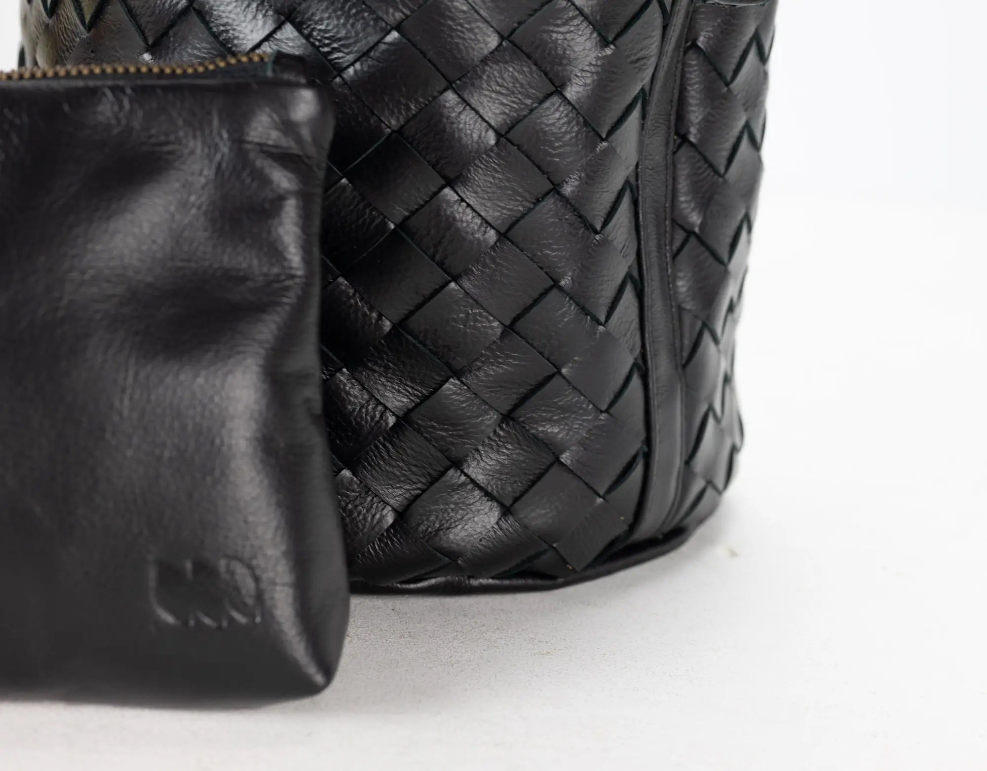 Black woven leather bag with a matching pouch on a light gray background