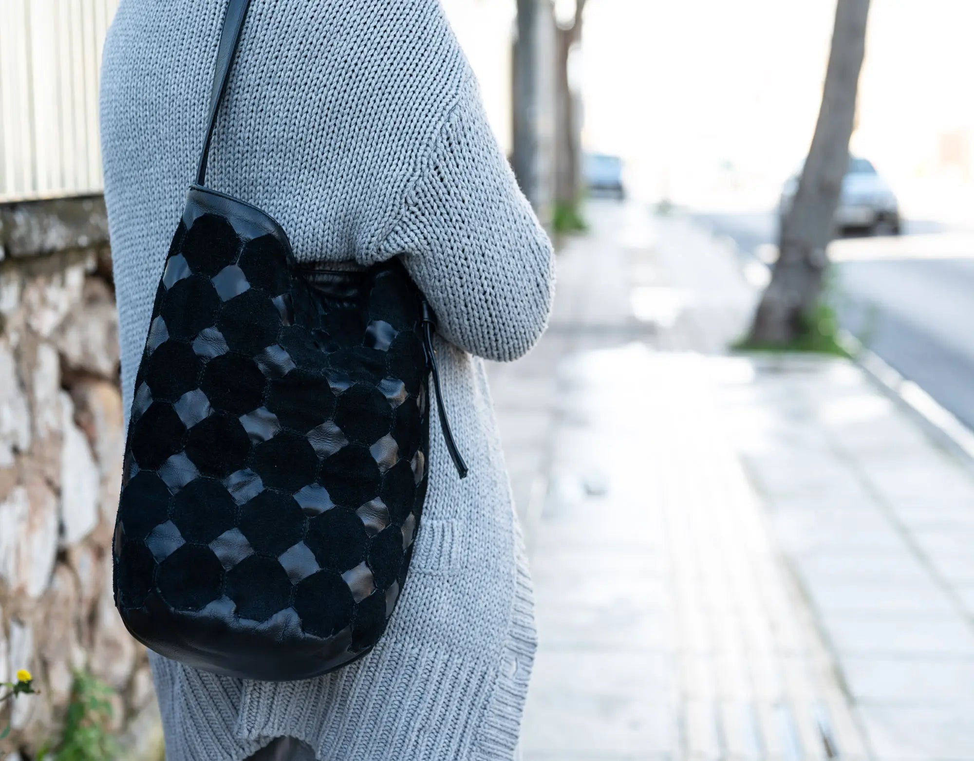 Person wearing a gray sweater holding a black checkered bag on a street.