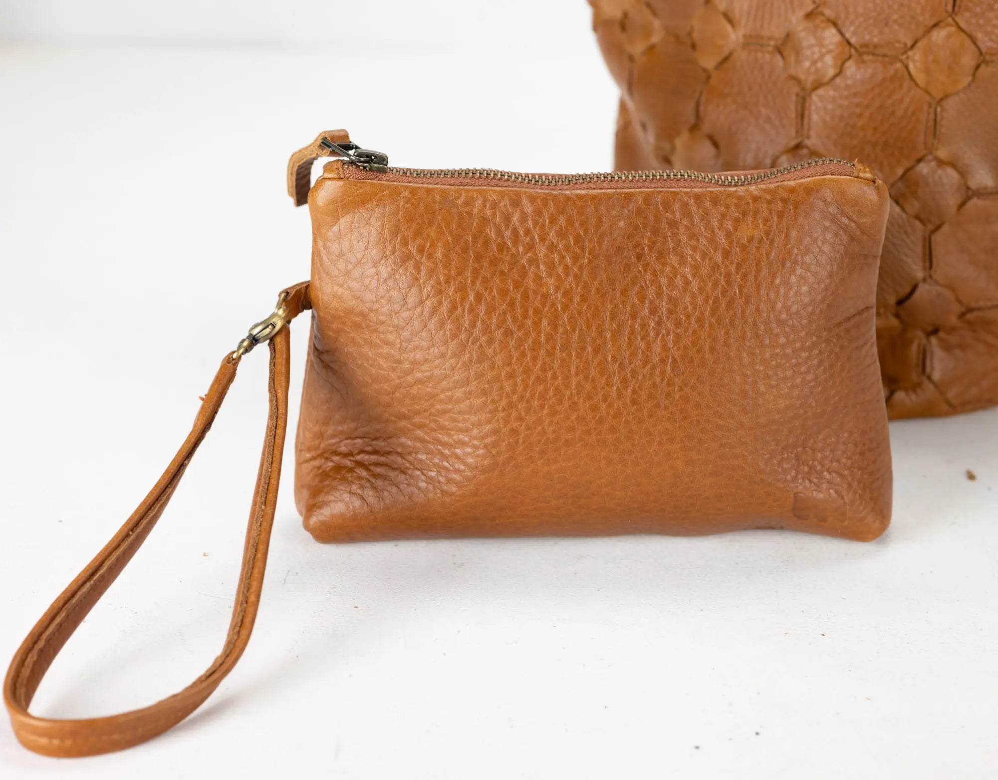 Brown leather clutch with wrist strap on a white background