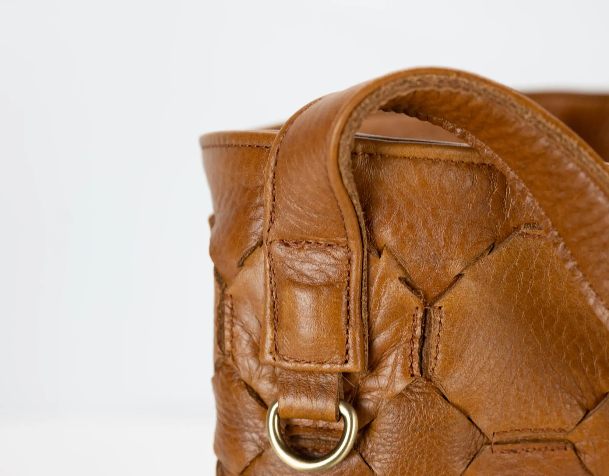 Close-up of a brown leather handbag with a gold ring on a white background