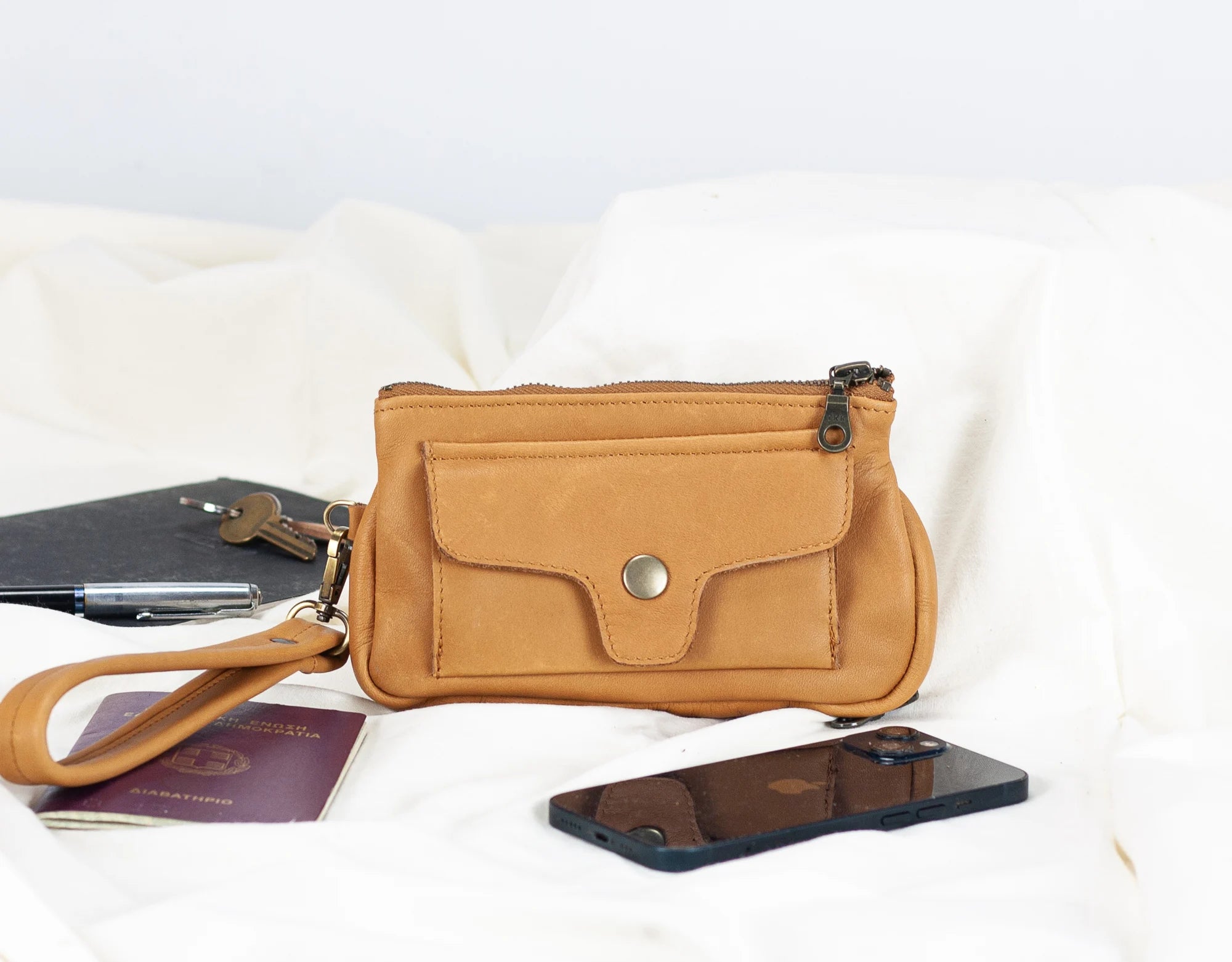 Tan wristlet bag with phone, passport, and pen on a white background