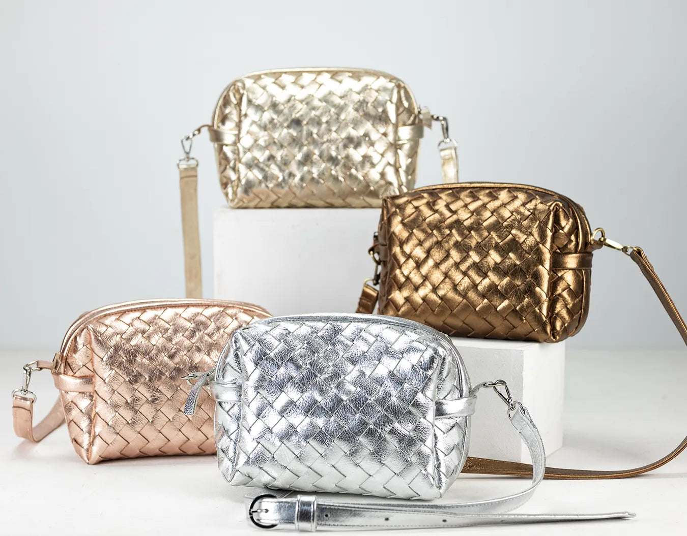 Four woven handbags in gold, silver, and rose gold on a light gray background