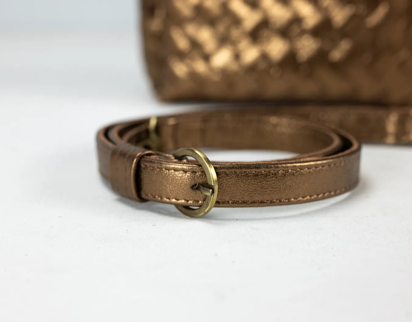 Brown leather strap with gold buckle in front of a brown textured bag on a white background