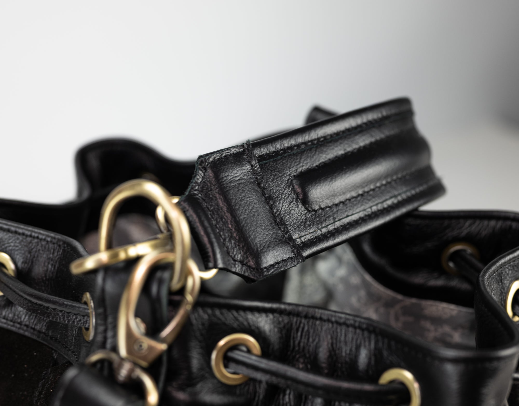 Close-up of black leather dog collars with gold hardware on a light gray background