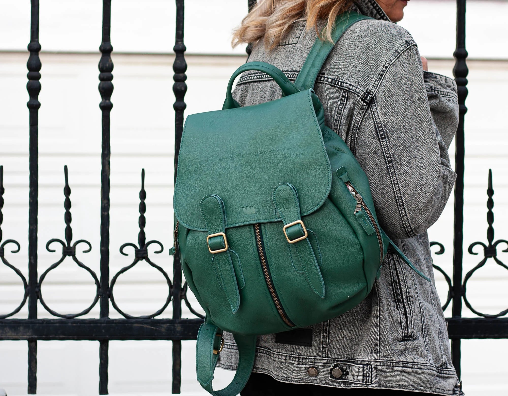Green backpack worn by a person against a black metal fence.