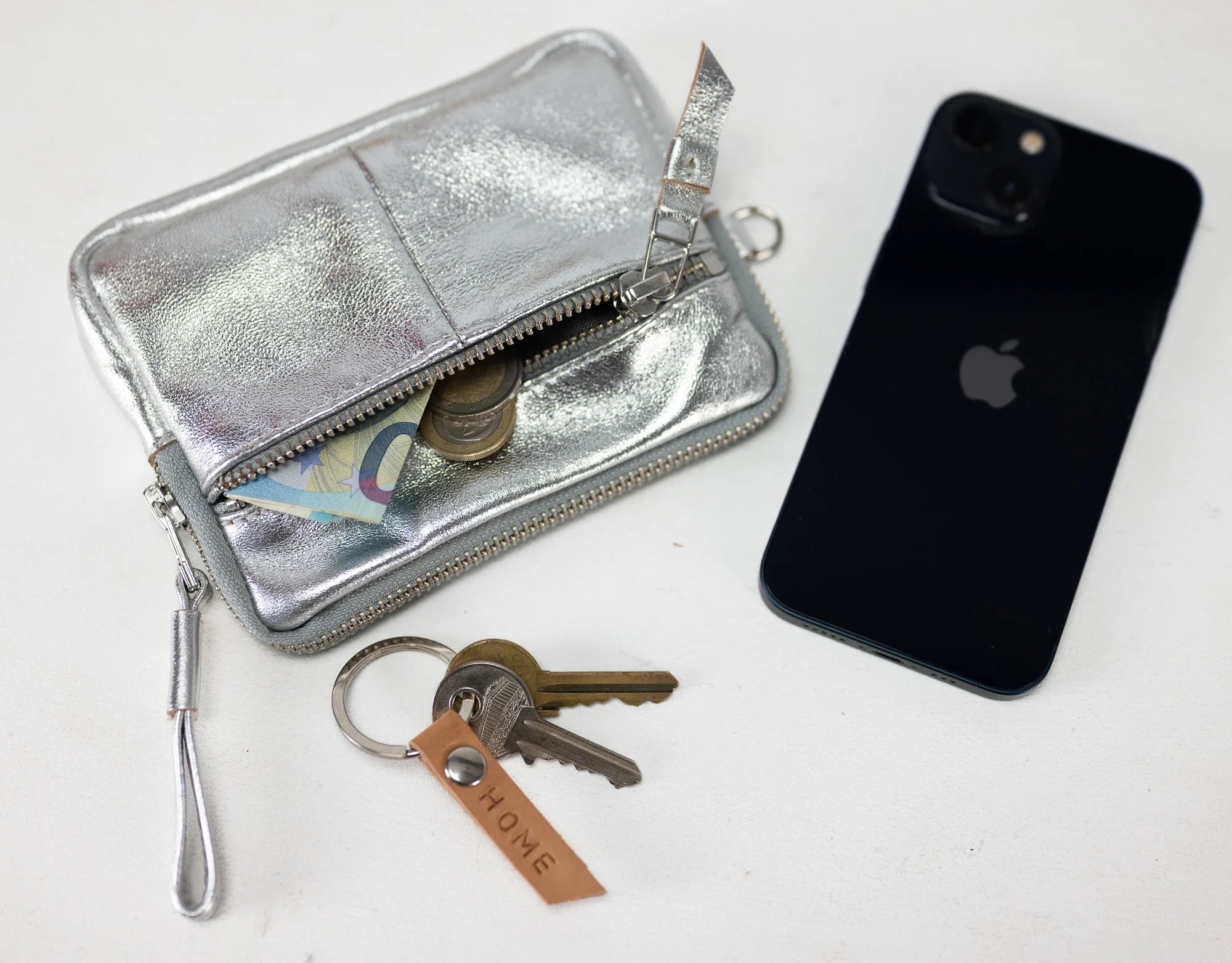 Silver wallet, keys, and black phone on a white background