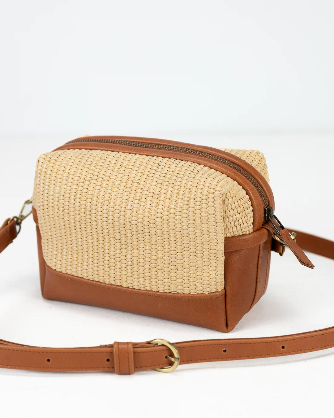 Beige woven bag with brown leather accents on a white background