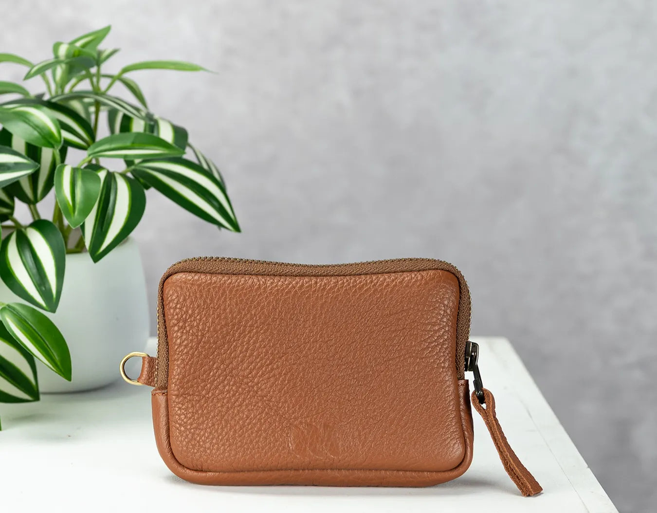 Brown leather wallet on a white surface with a plant in the background