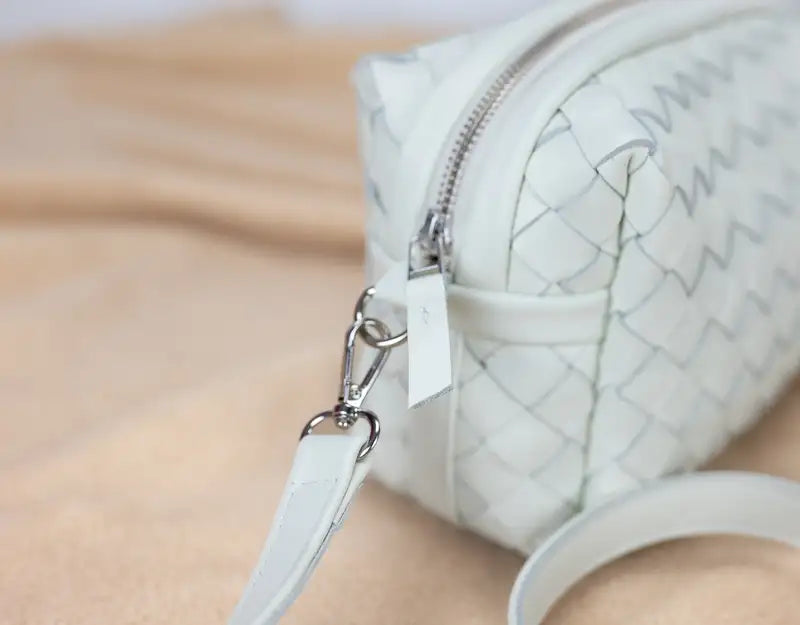 White quilted handbag with a zipper on a beige surface