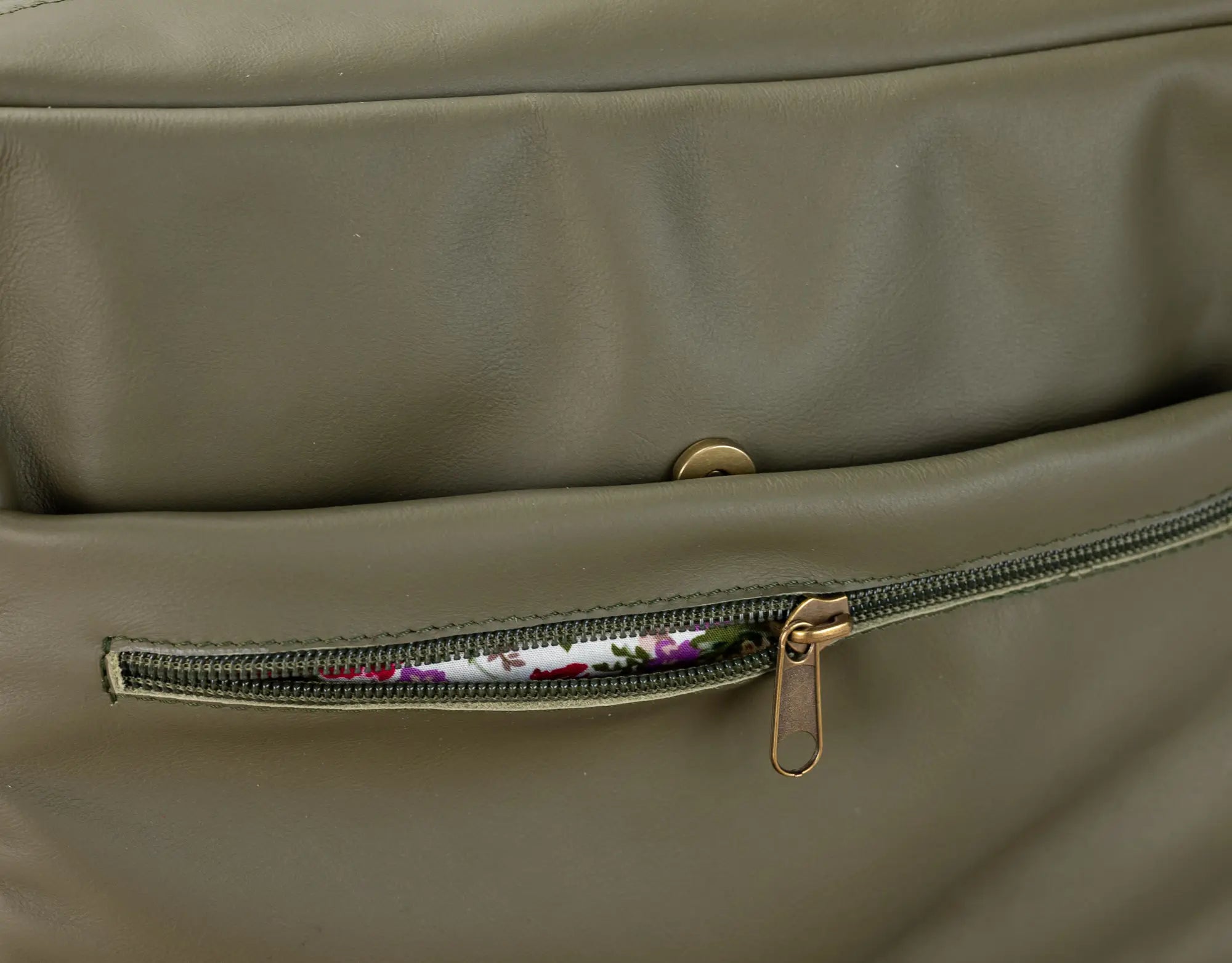 Close-up of a green leather bag with a floral patterned interior visible through a zipper.