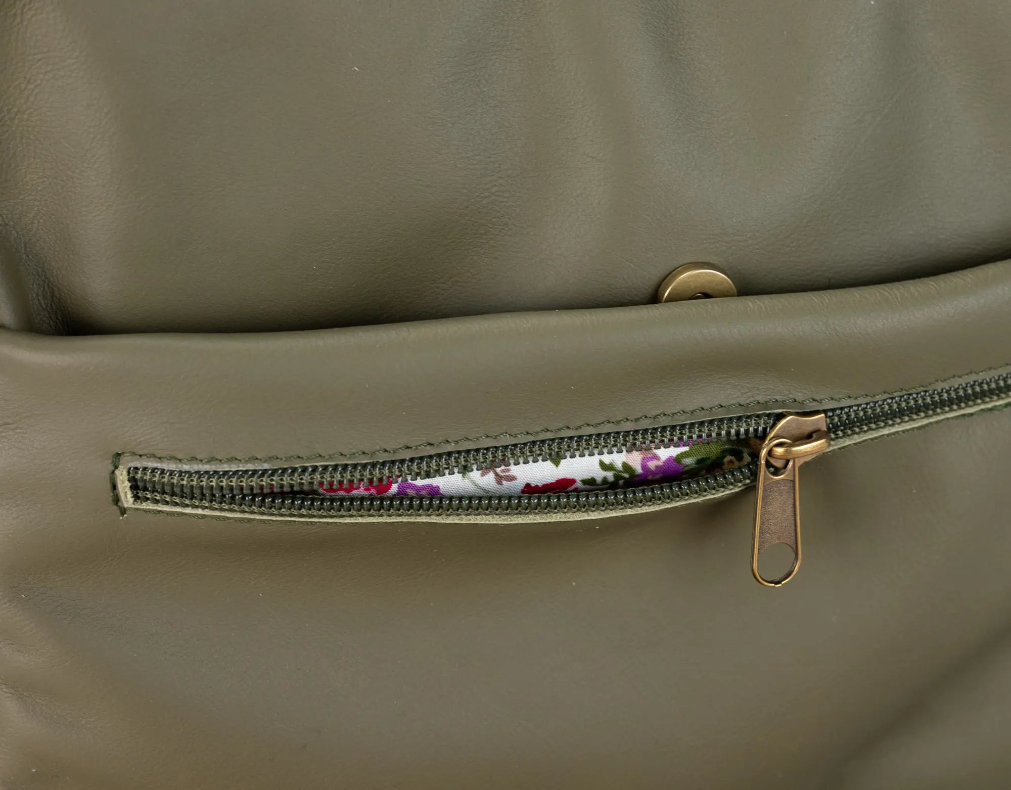 Close-up of a green leather bag with a zipper pocket showing floral lining.