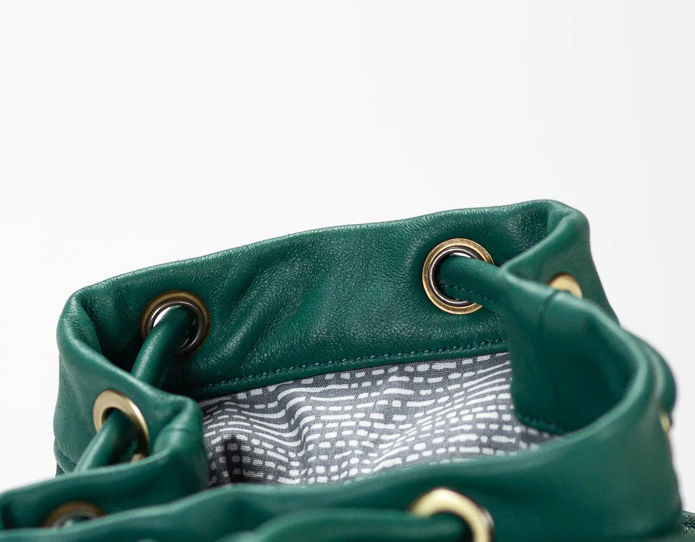 Close-up of a green leather bag with gold eyelets on a white background