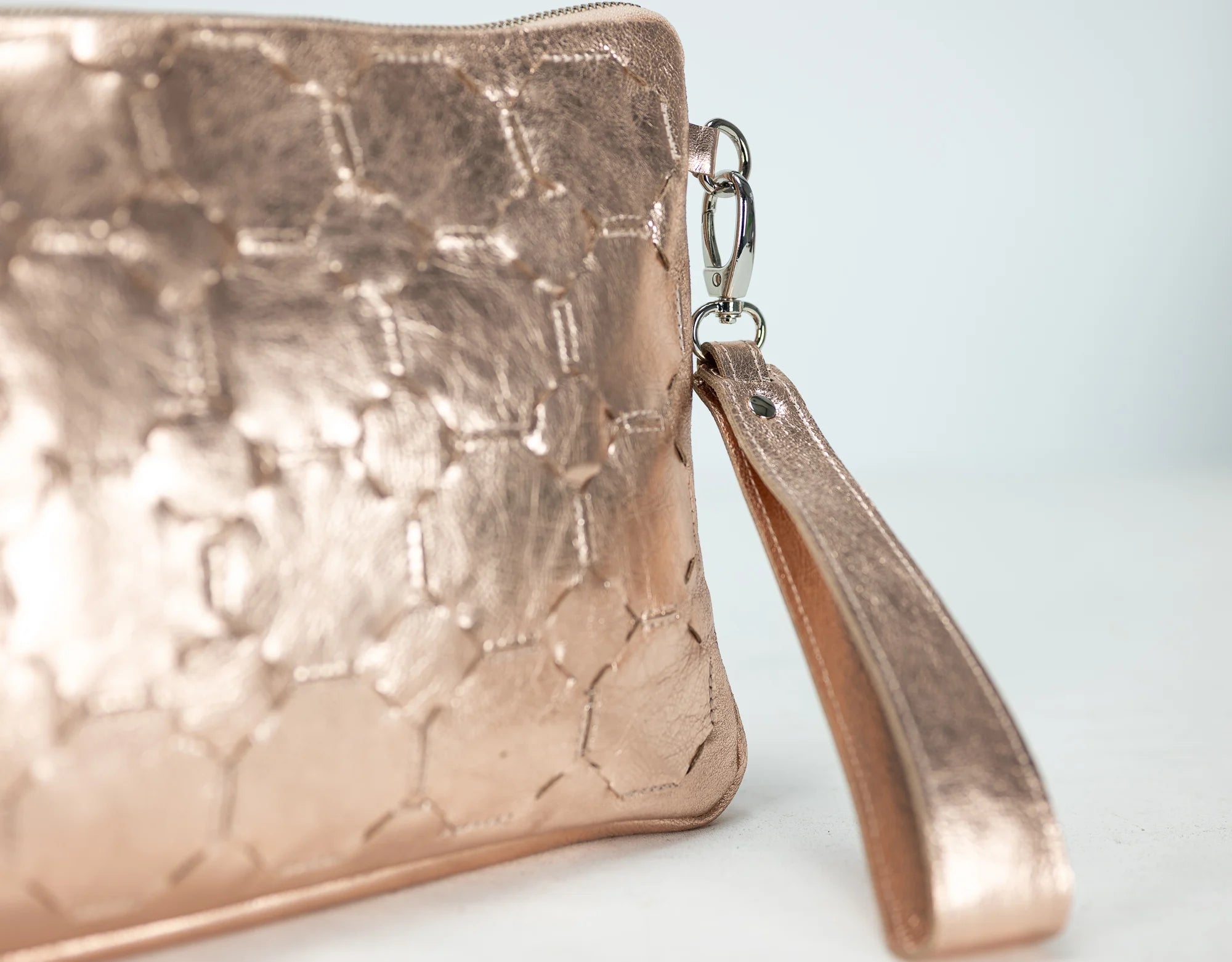 Rose gold textured clutch bag with a matching strap on a light background