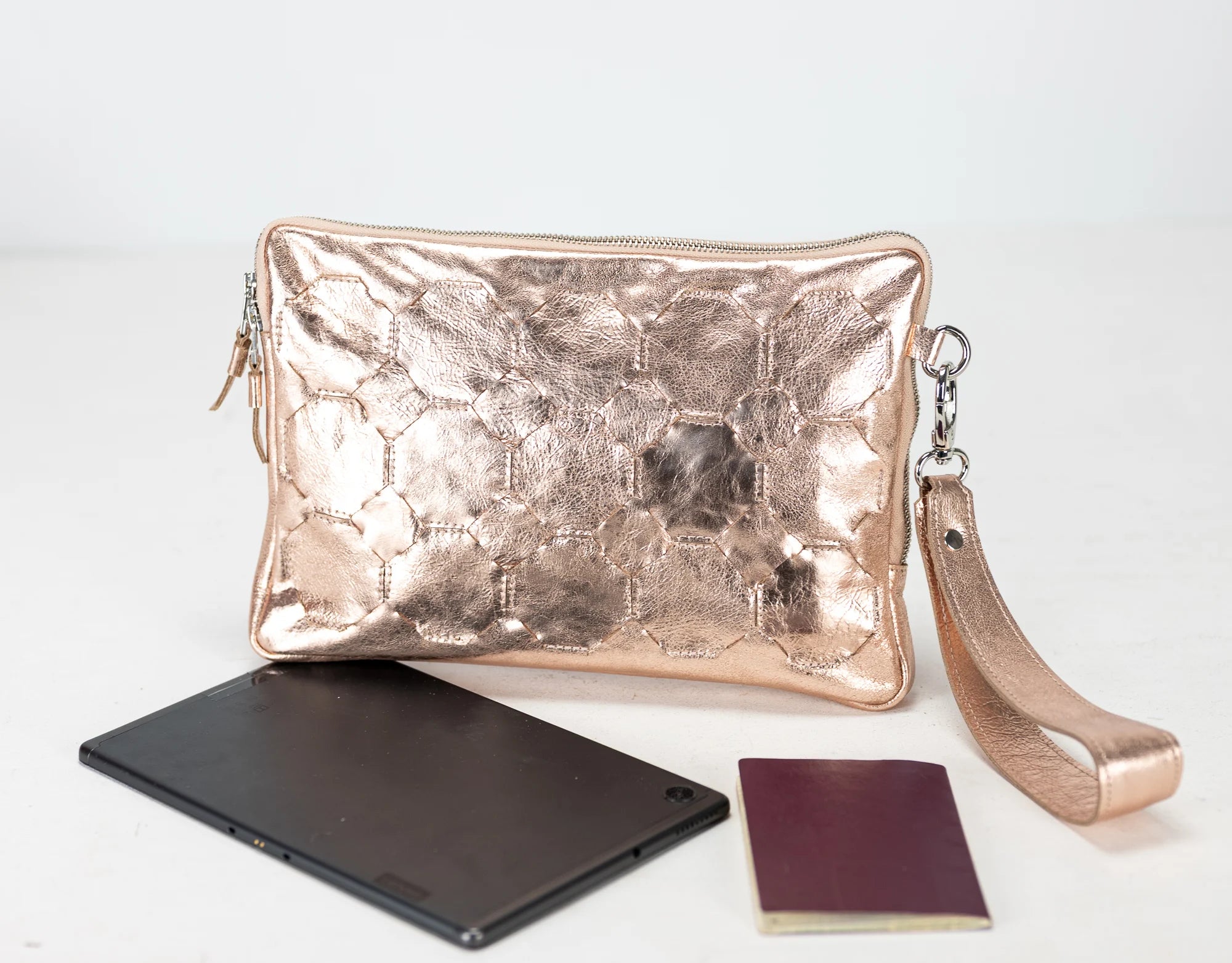 Rose gold clutch bag with a phone and book on a white background
