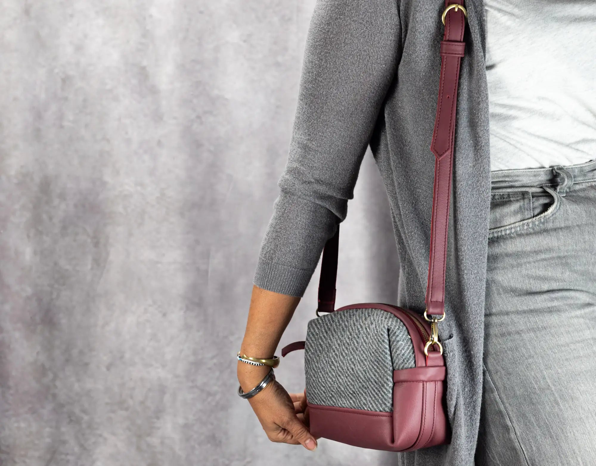 Person holding a maroon crossbody bag with a gray background
