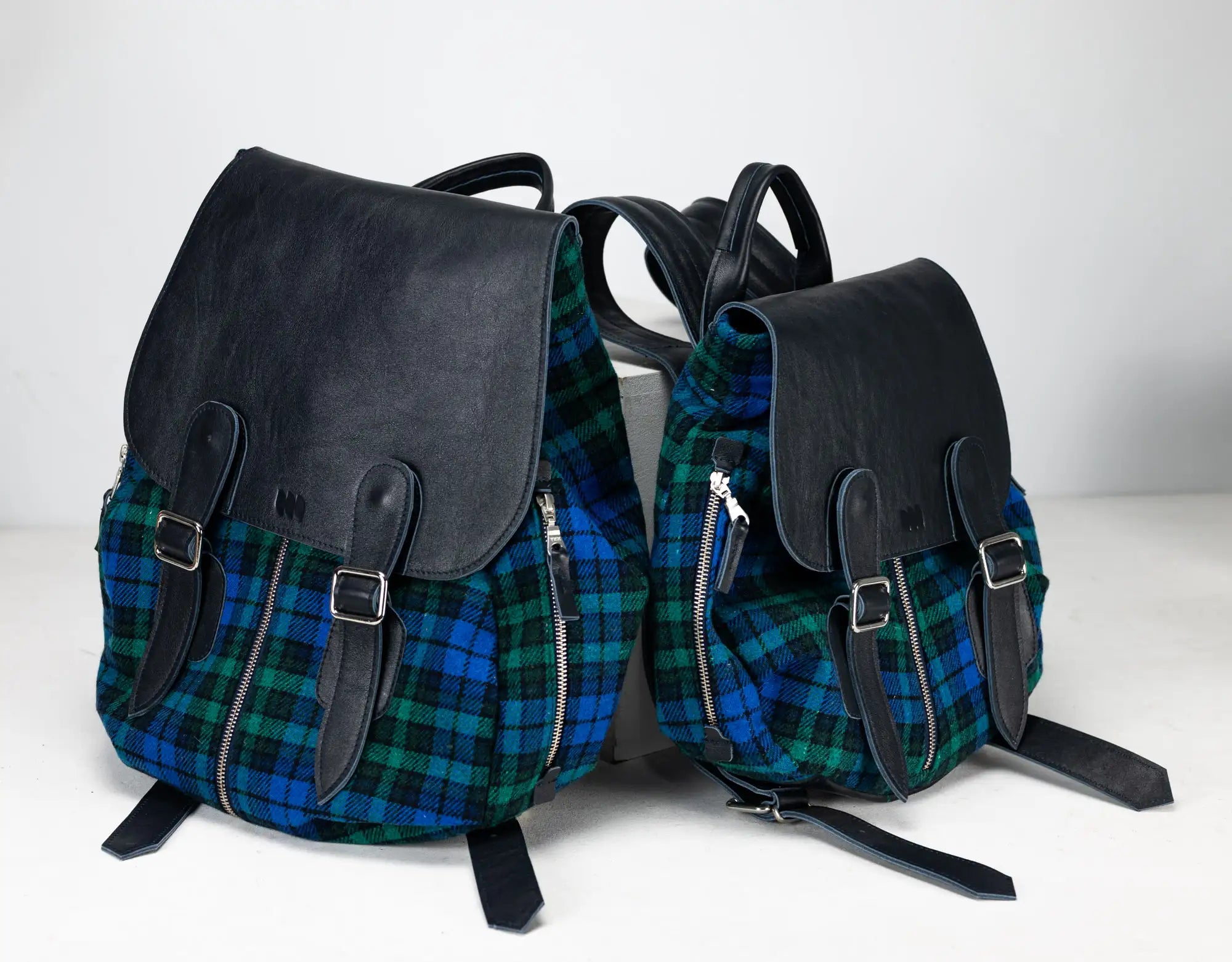 Two backpacks with plaid pattern and black leather accents on a white background