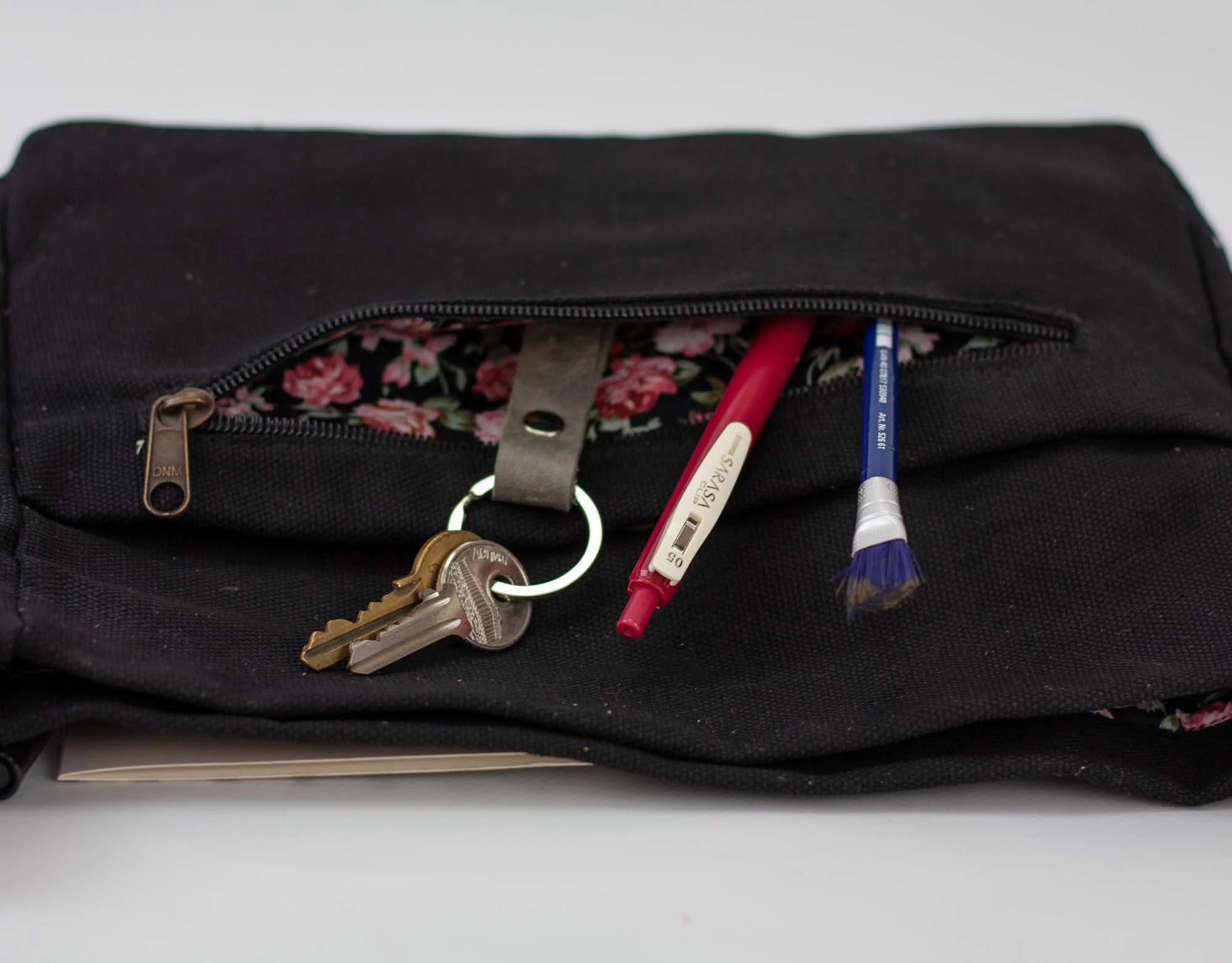 Black pouch with keys and pens peeking out on a light gray background