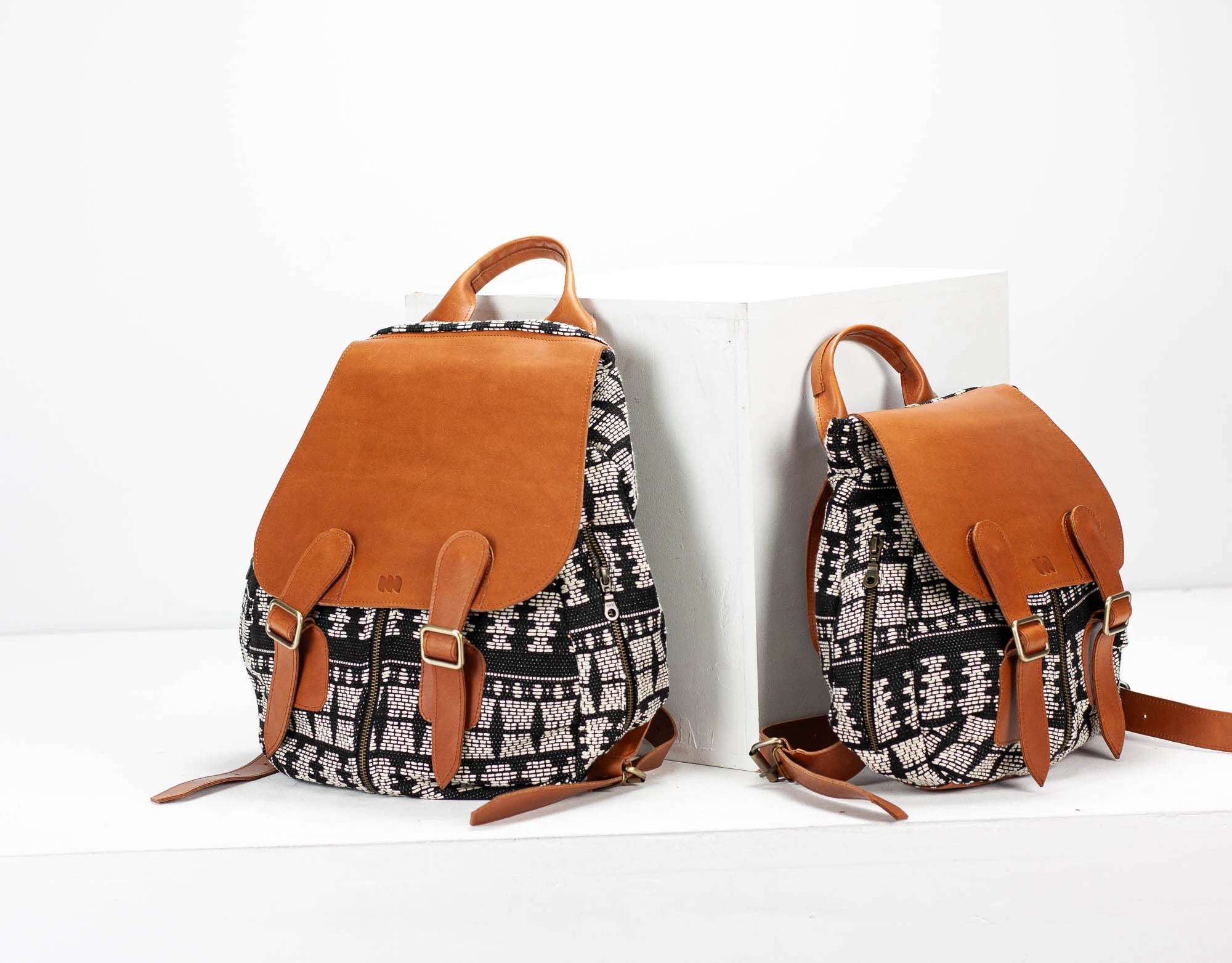 Two backpacks with patterned fabric and brown leather straps on a white background