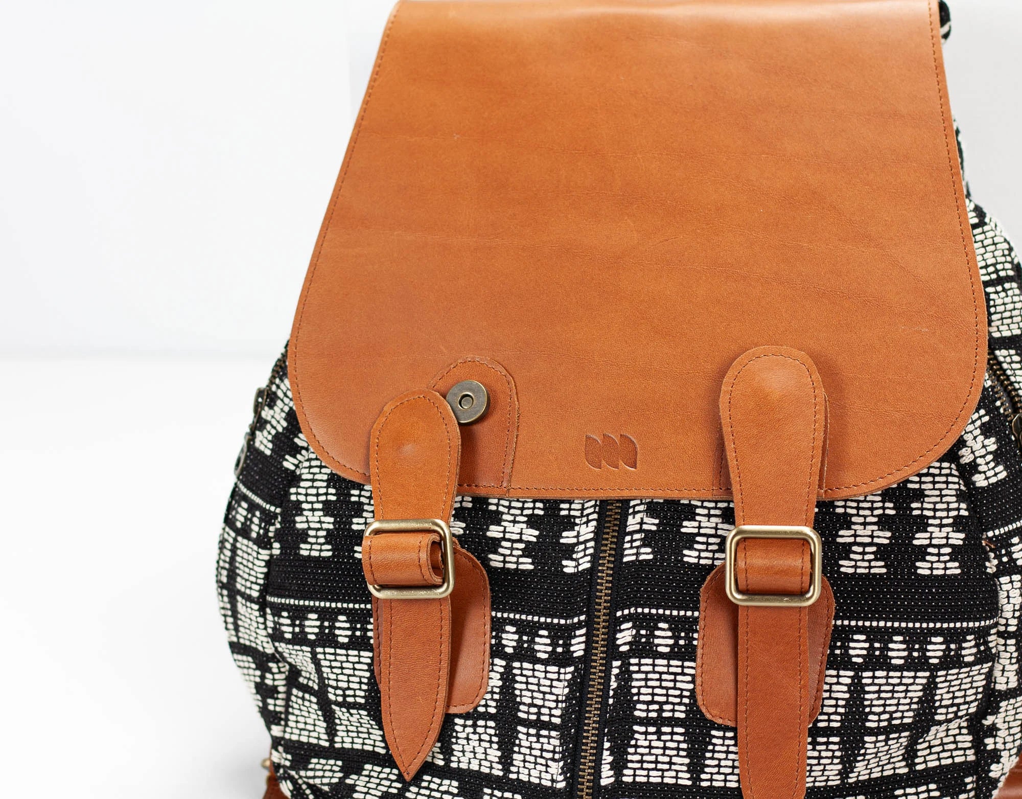 Backpack with brown leather straps and patterned fabric body on a white background