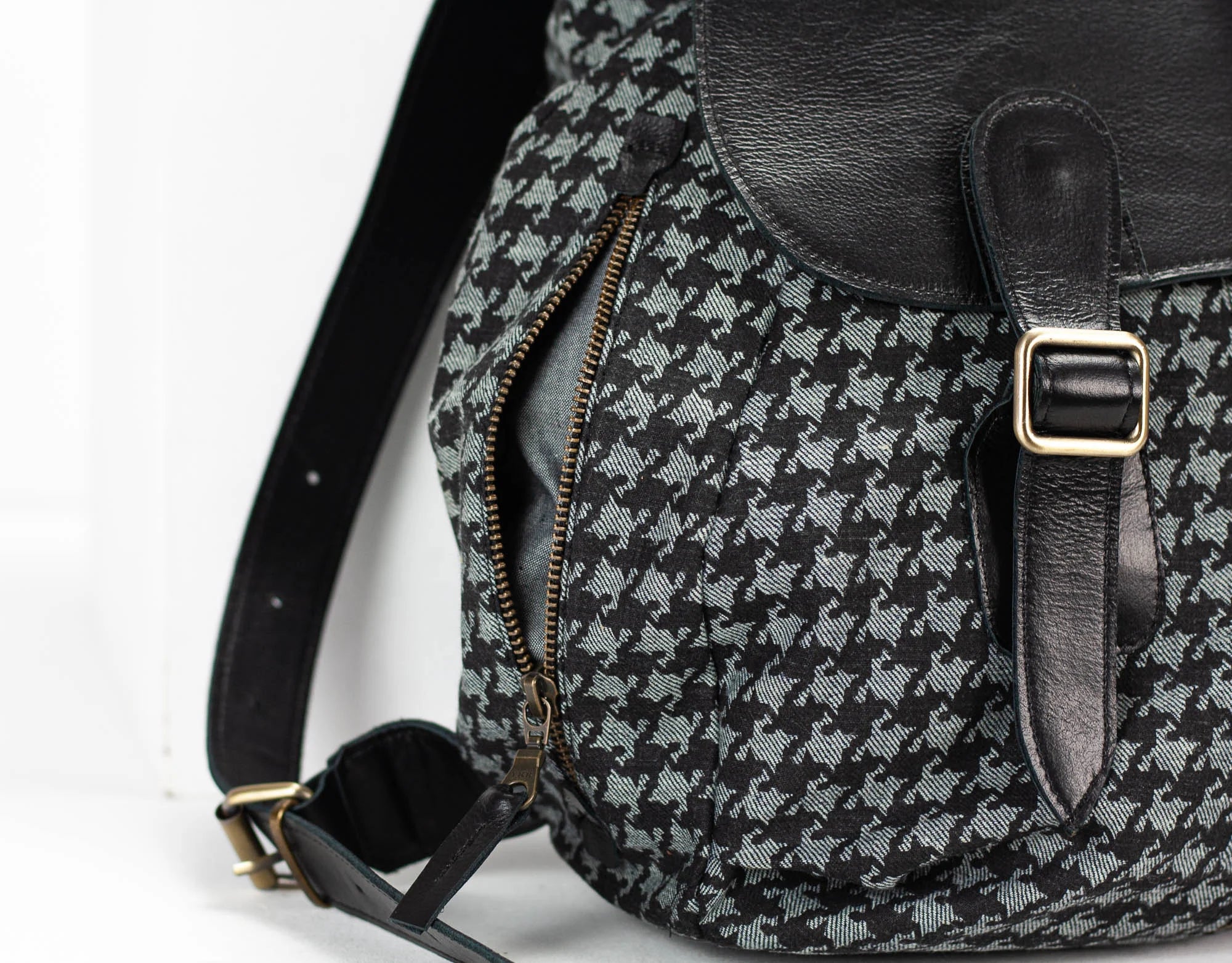 Black and gray houndstooth patterned backpack with a gold buckle on a white background