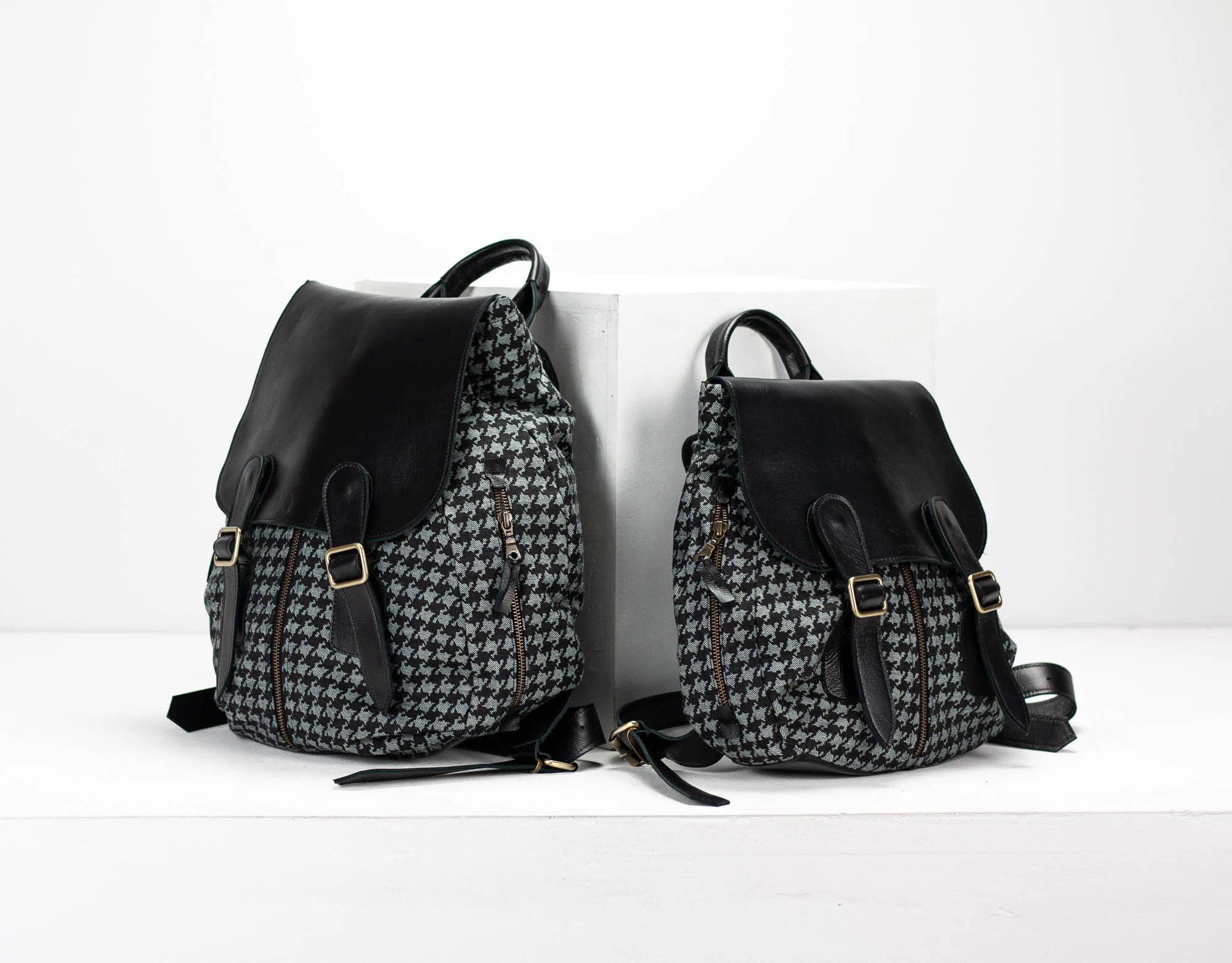 Two backpacks, one with a houndstooth pattern and the other black, on a white background.