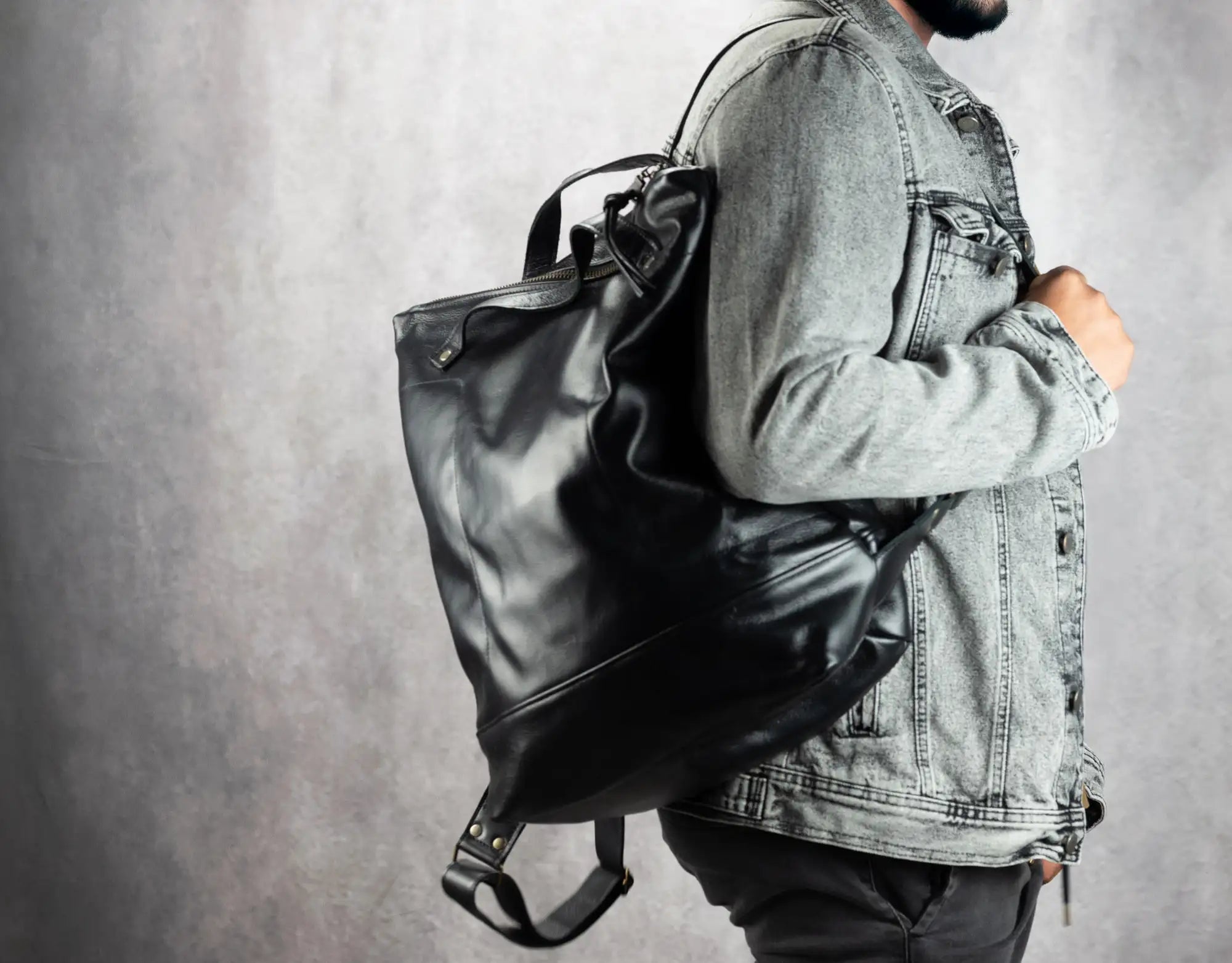 Person wearing a large black leather backpack against a gray background