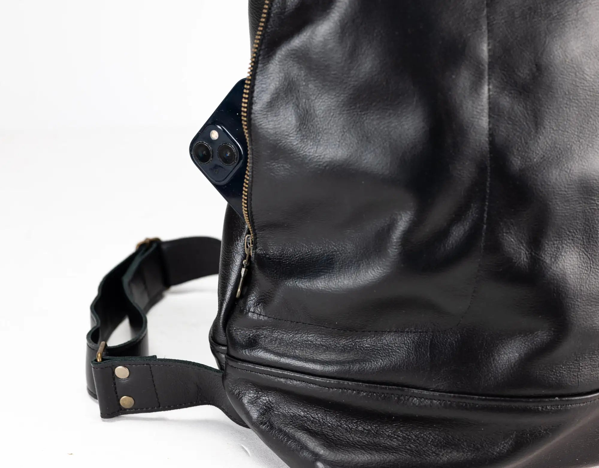 Close-up of a black leather bag with a strap on a white background