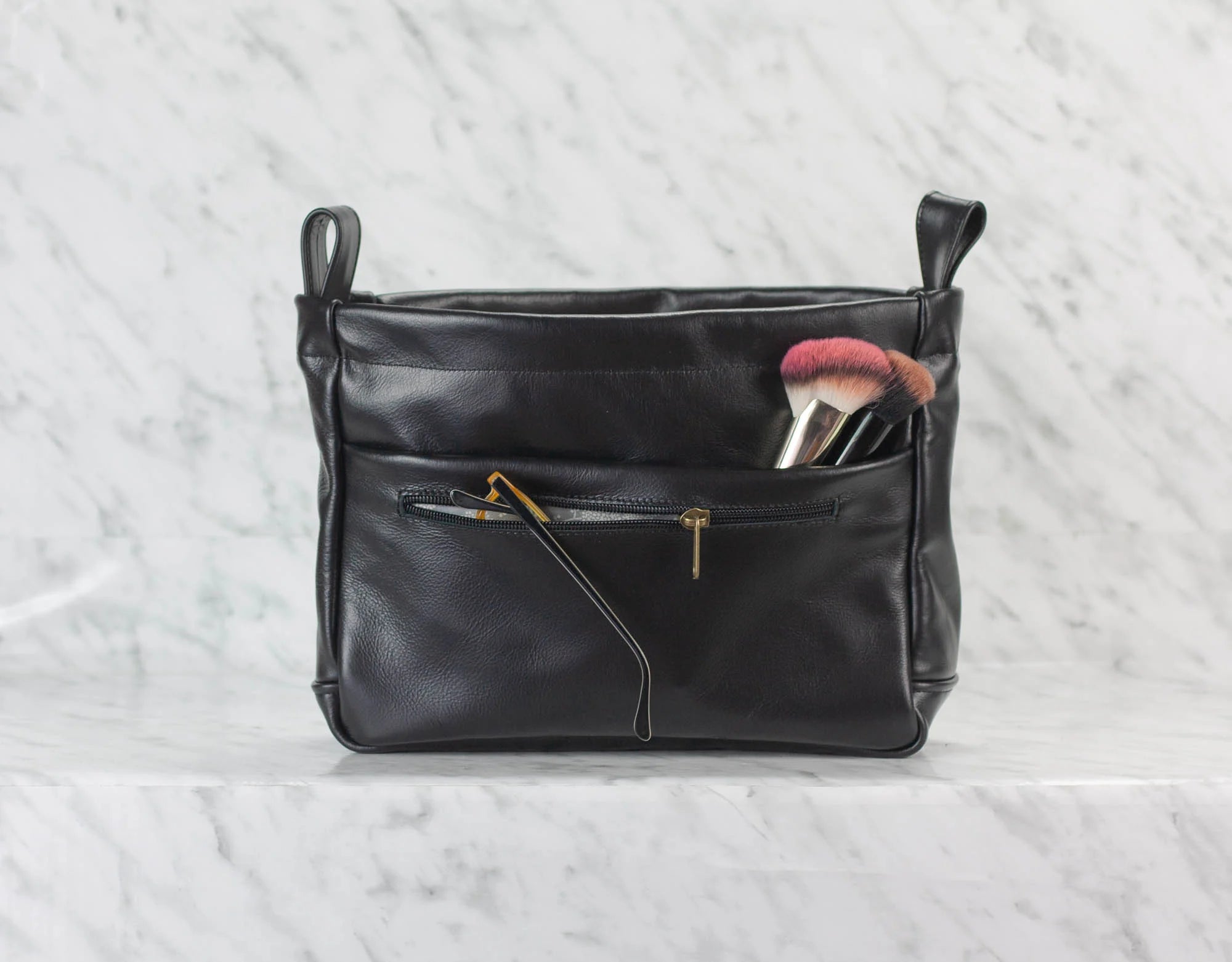 Black leather handbag with makeup brushes on a light gray background