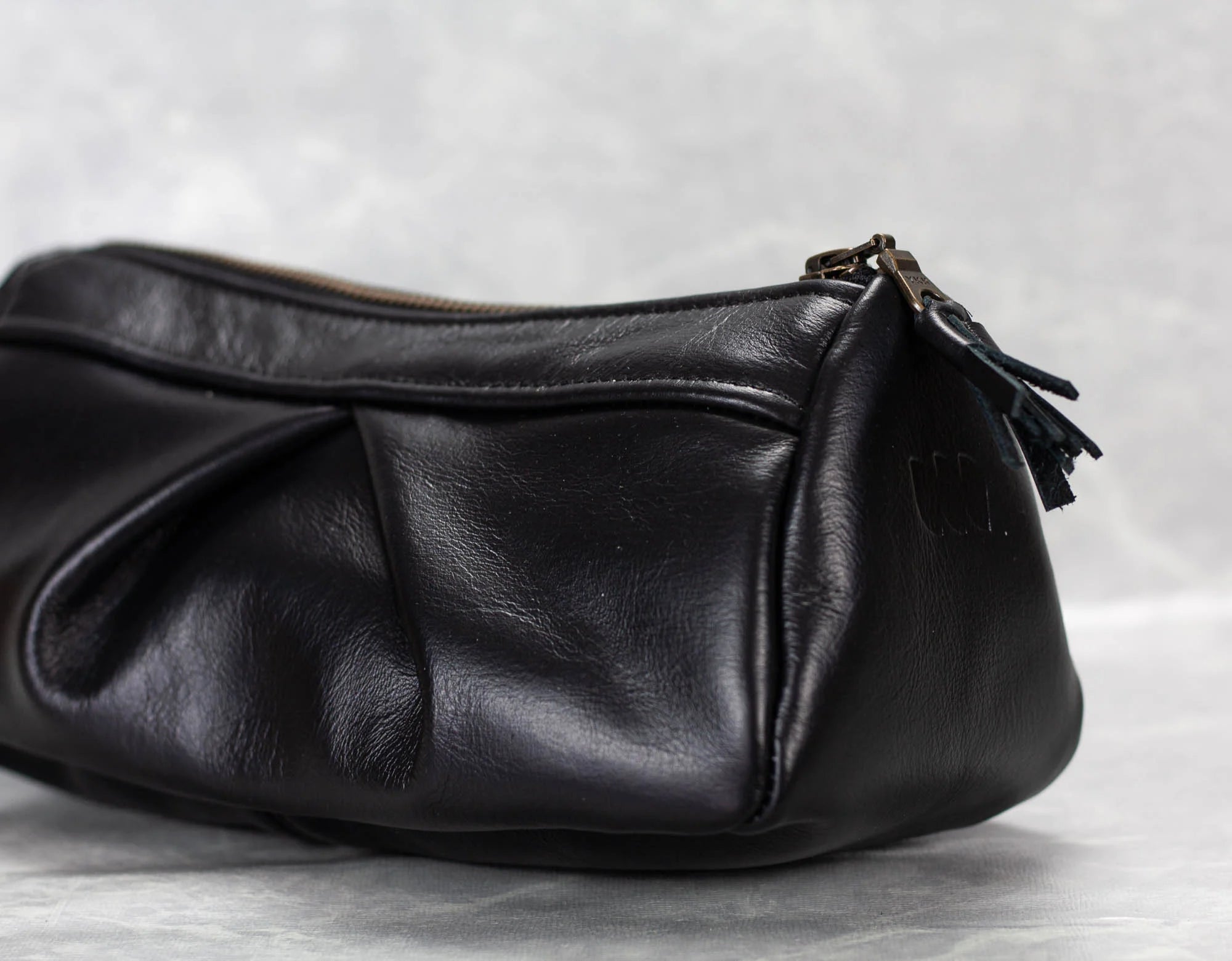 Black leather handbag with a zipper on a light gray background