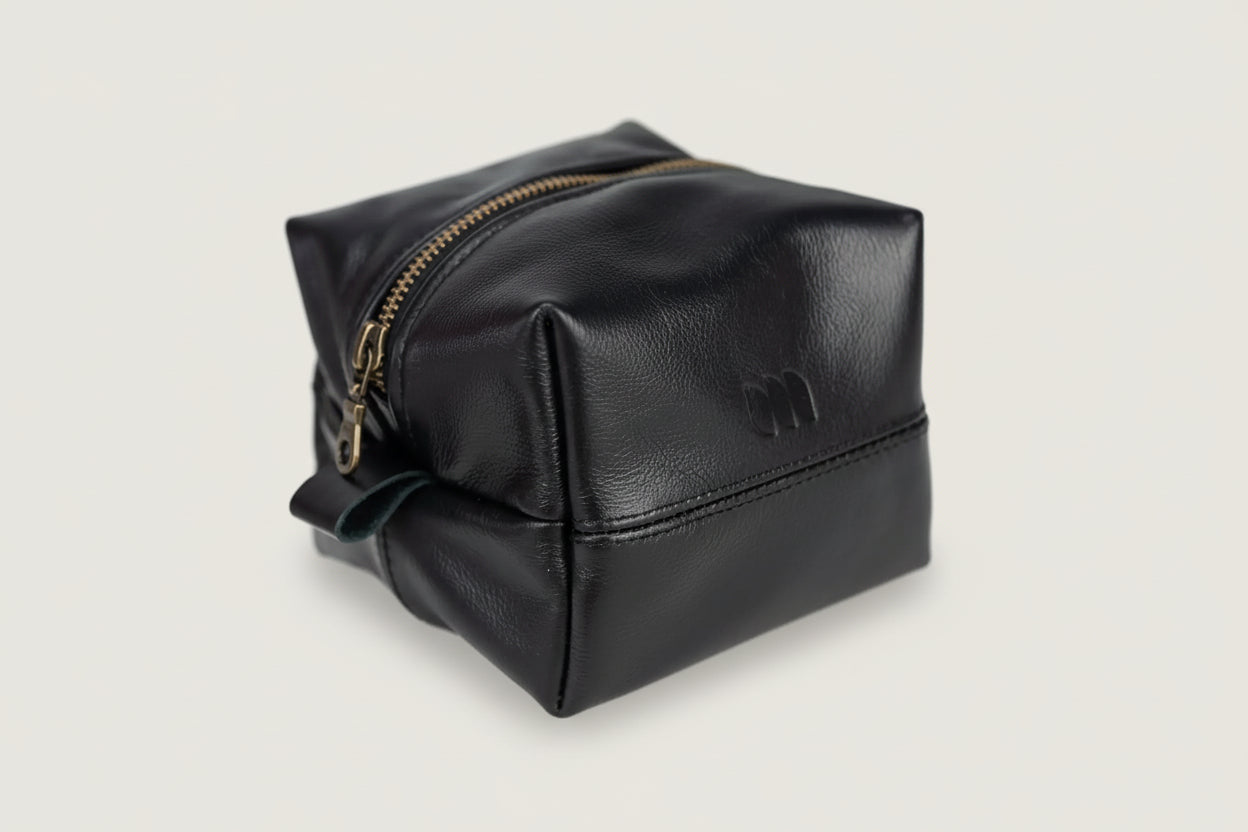 Black leather toiletry bag with gold zipper on a white background