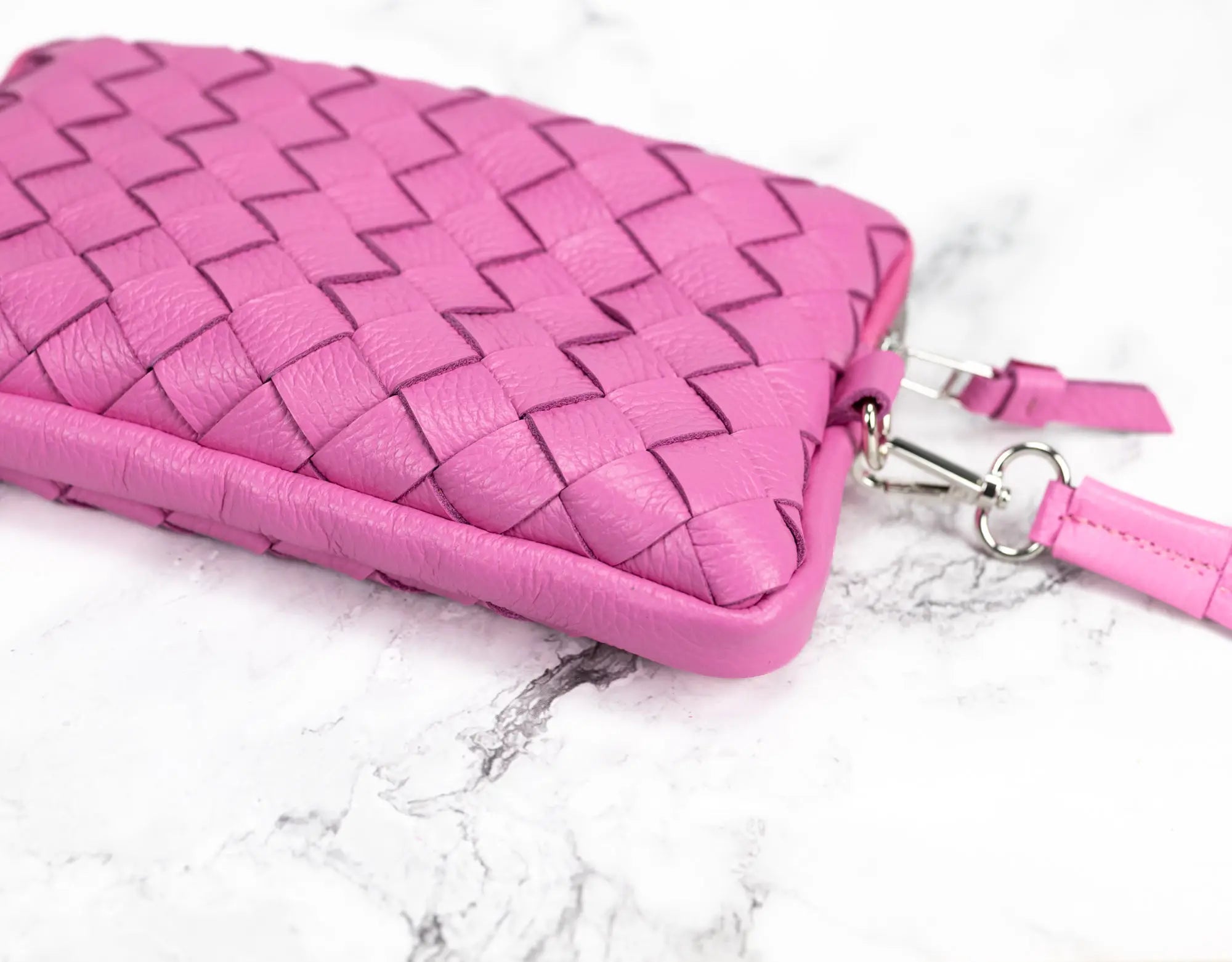 Pink woven handbag with a strap on a marble surface