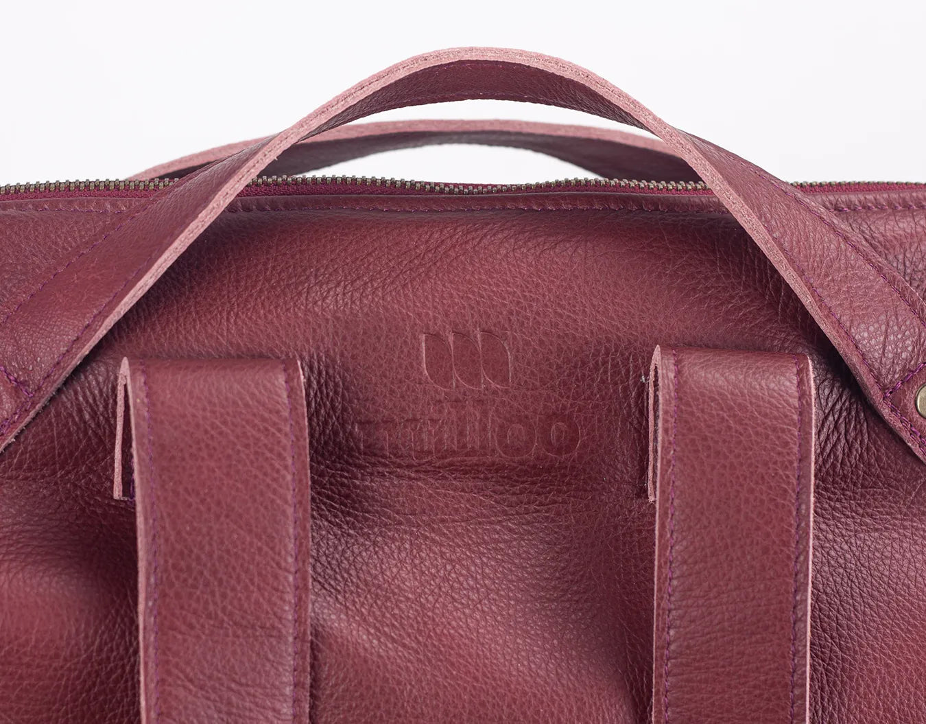 Close-up of a maroon leather bag with visible branding on a white background