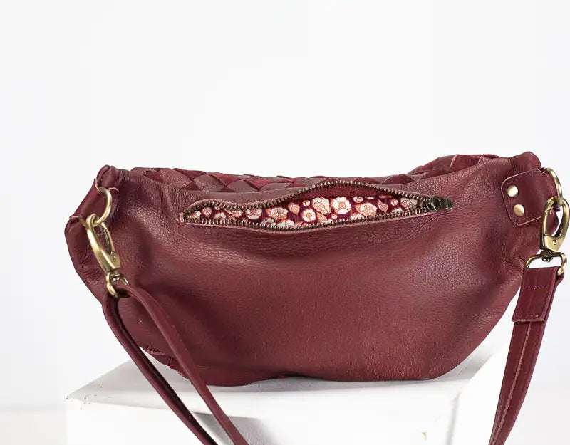 Maroon handbag with floral zipper pull on a white background