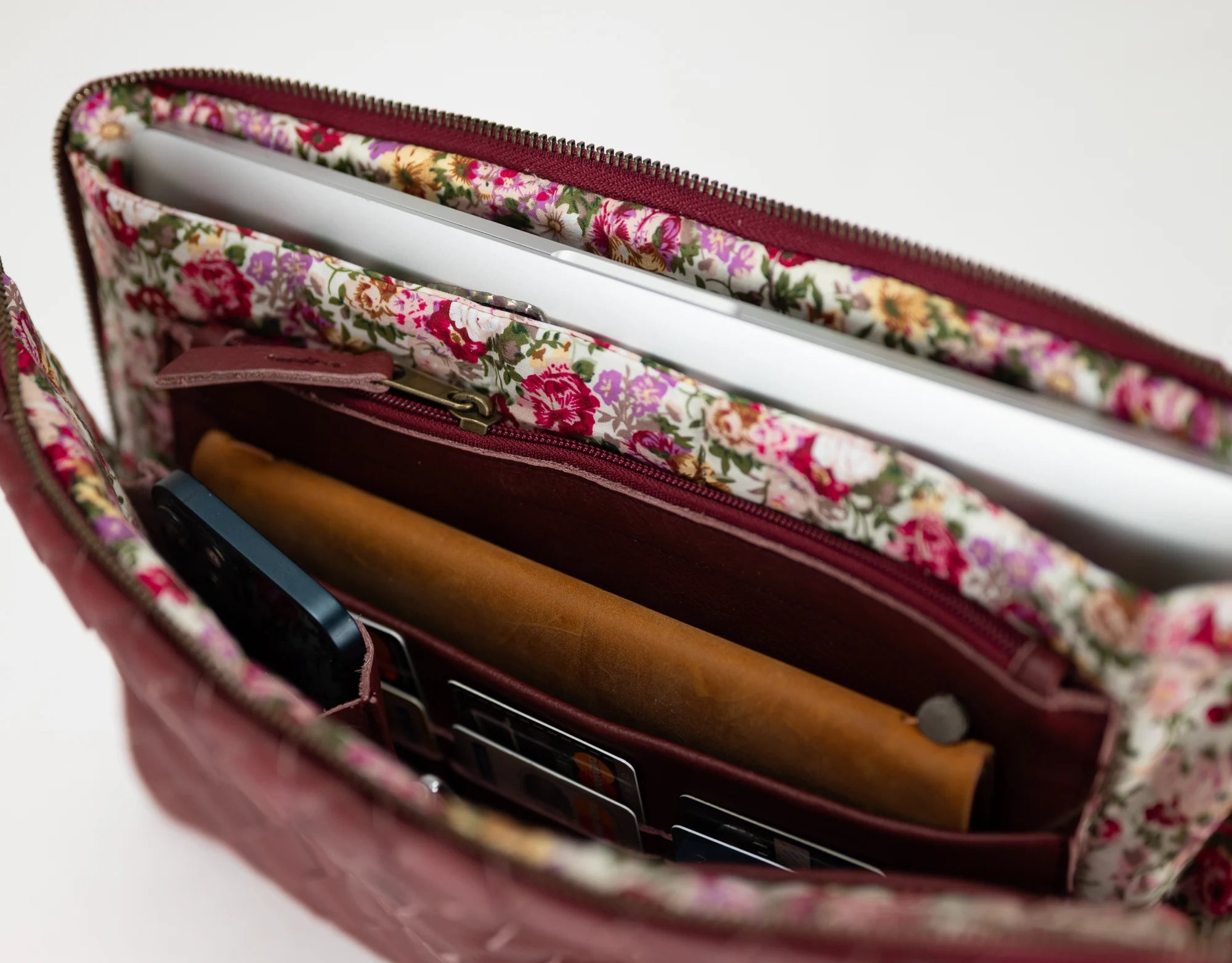 Floral-patterned interior of a maroon handbag with a phone and brown item inside.