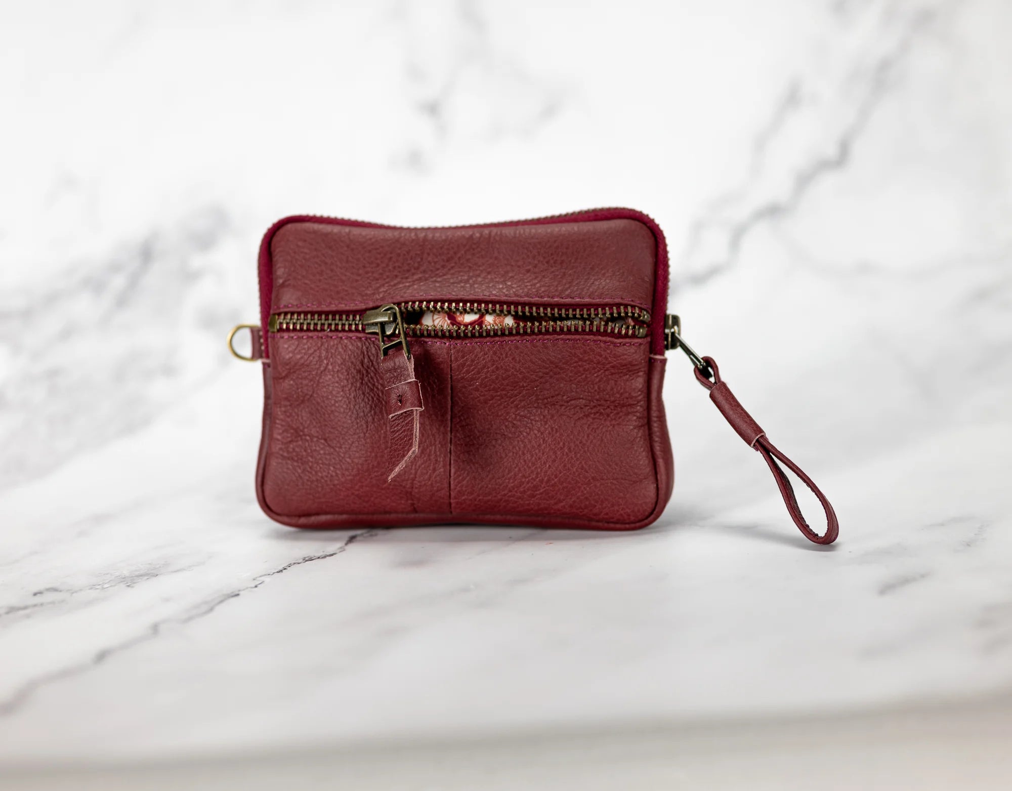 Red leather wristlet with a zipper on a marble surface
