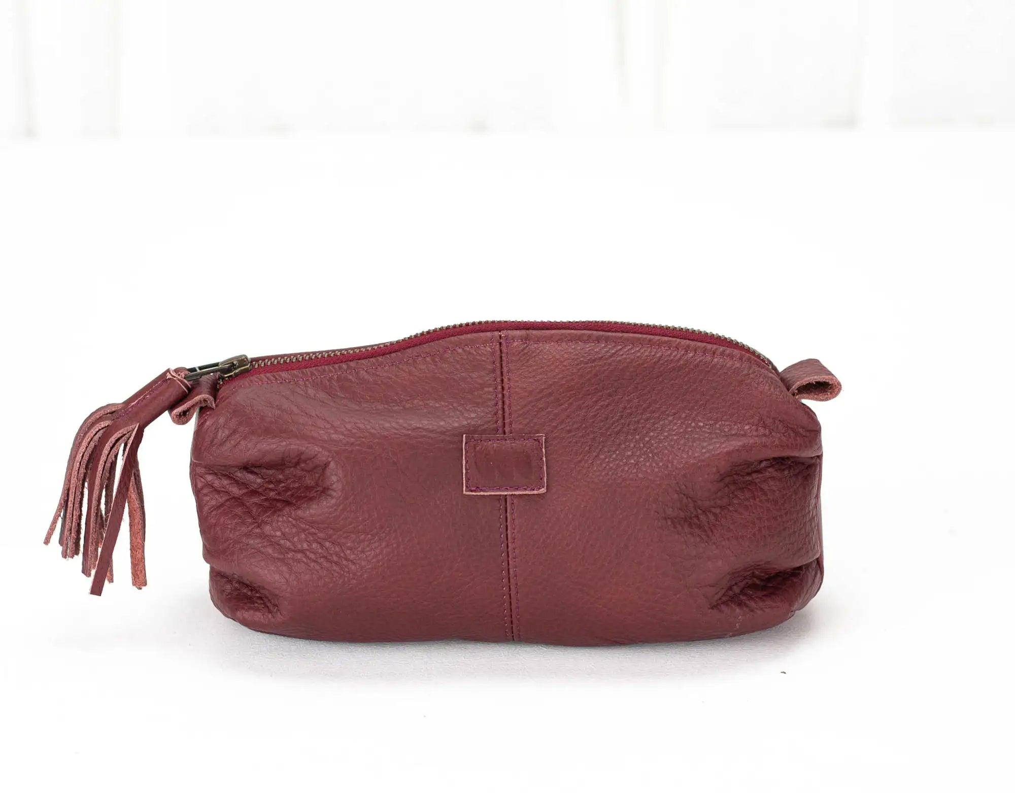 Maroon leather pouch with a zipper and tassel on a white background