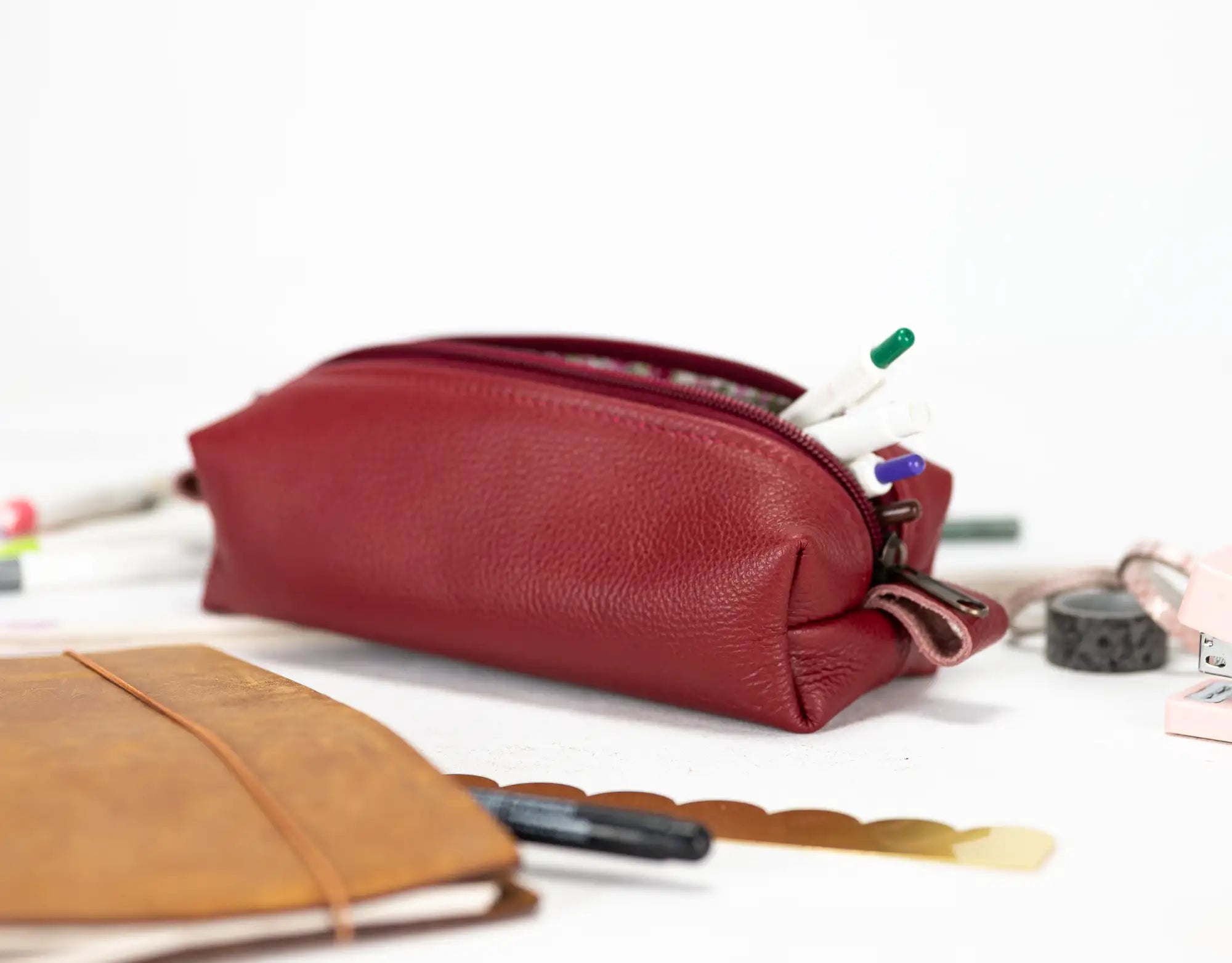 Red leather pencil case with stationery items on a white surface