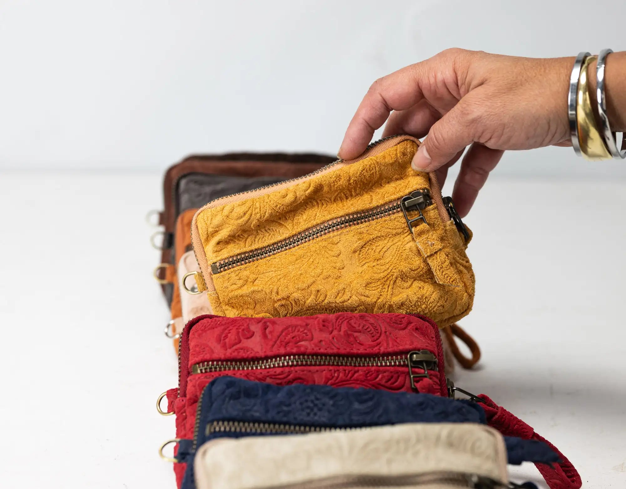 Stack of colorful leather wallets with a hand reaching to open one, on a light background