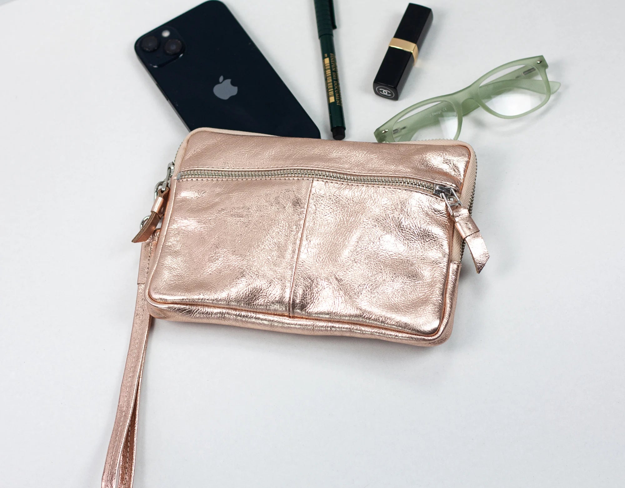 Rose gold crossbody bag with phone, pen, and glasses on a light background
