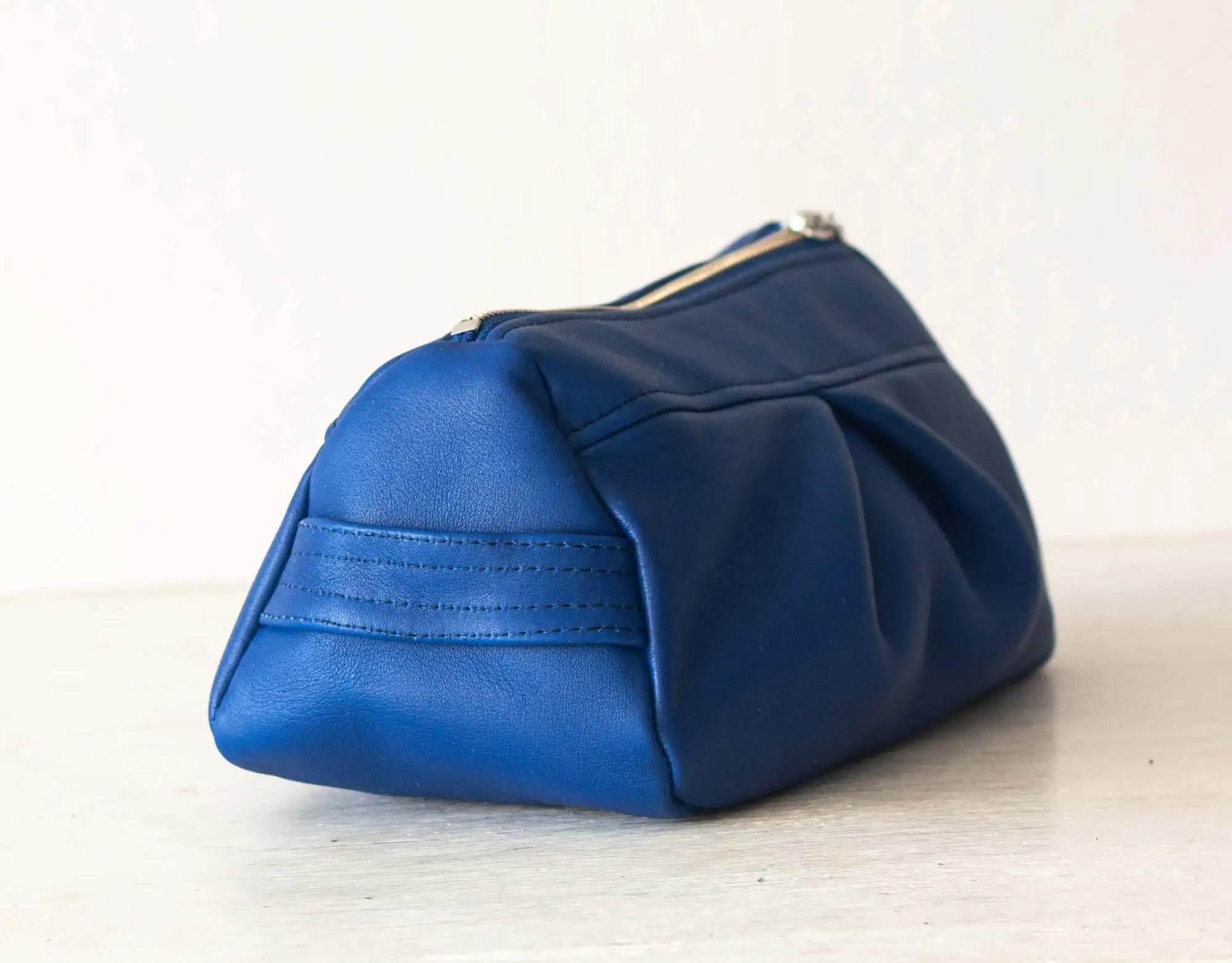 Blue leather pouch on a light wooden surface with a white background