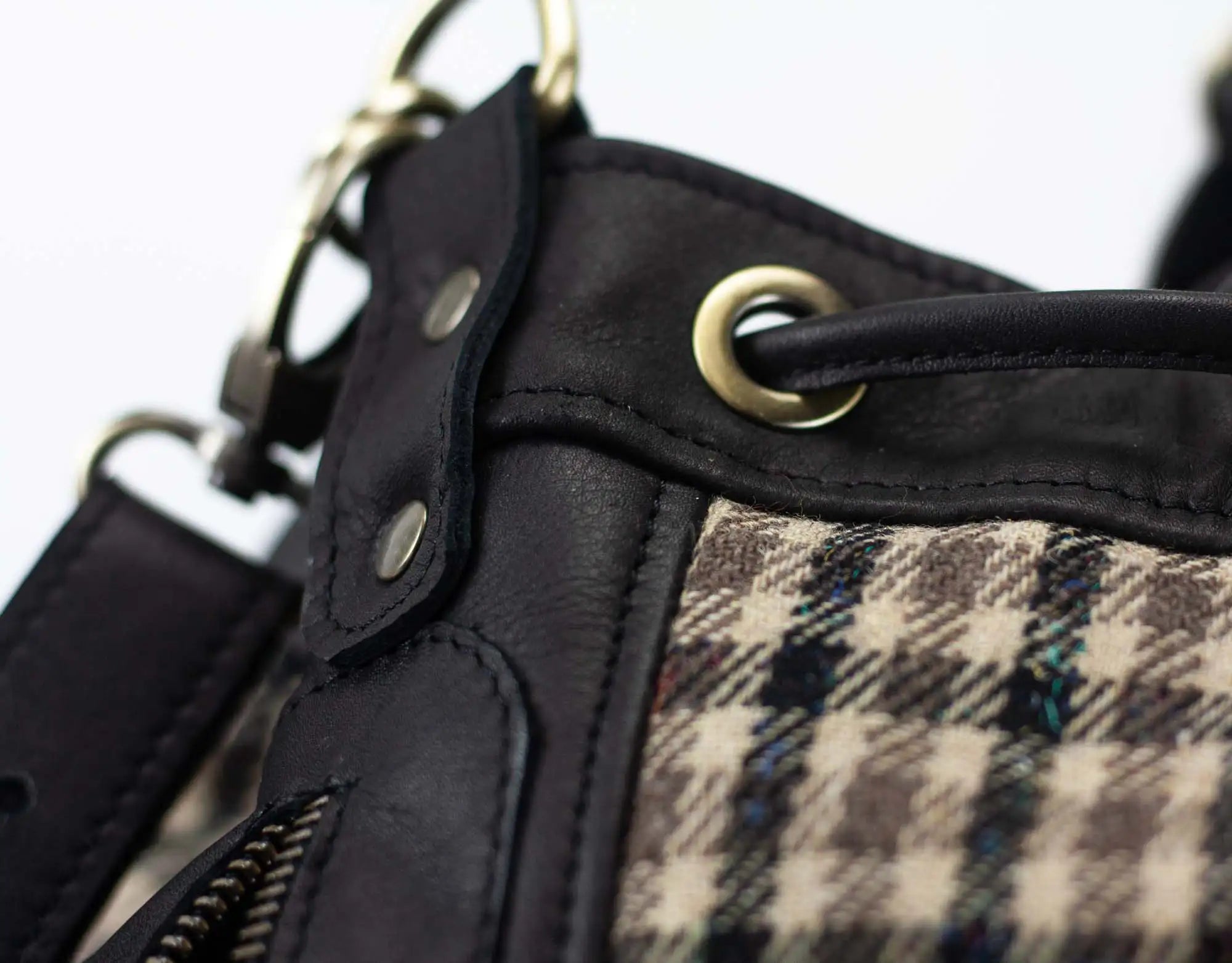 Close-up of a black leather and plaid fabric bag with metal hardware.