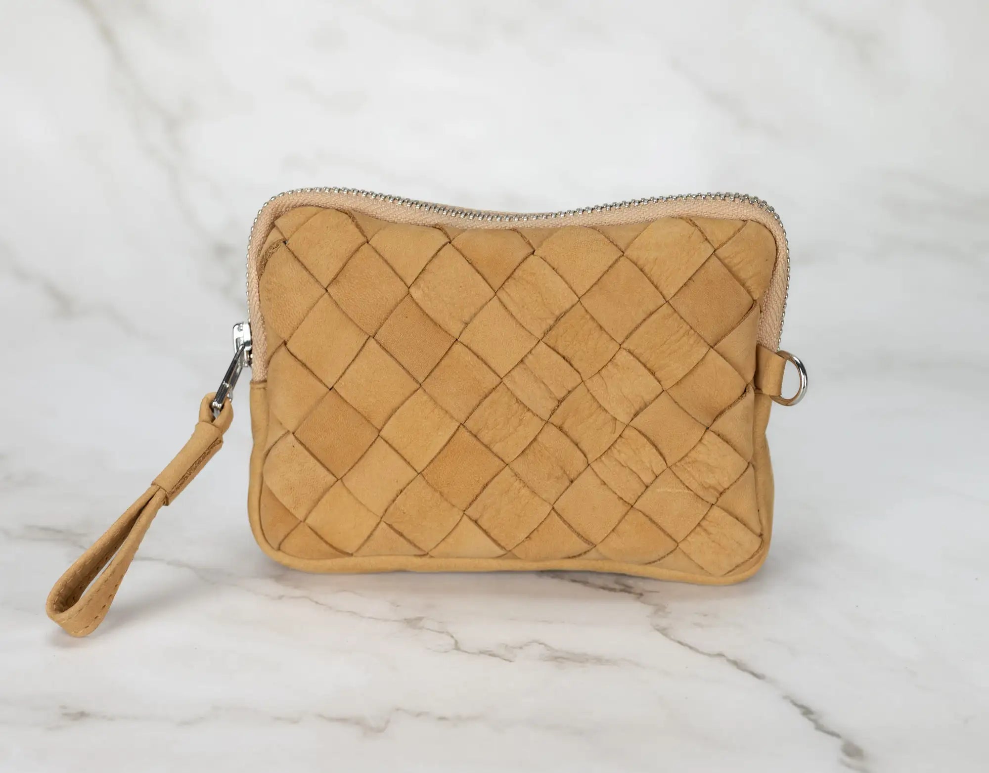 Quilted beige pouch with a strap on a marble surface