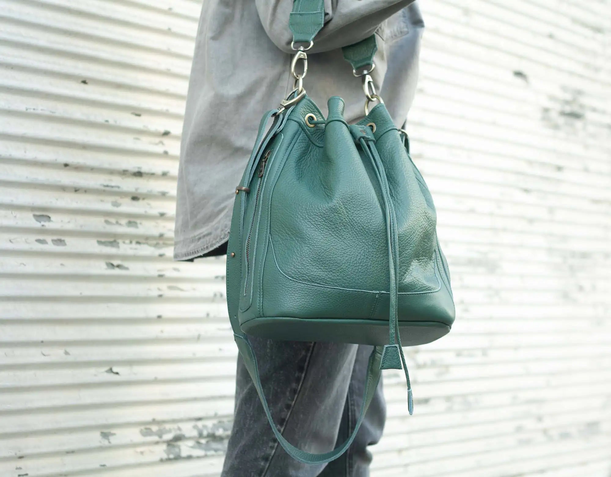 Green leather backpack held by a person against a textured white background
