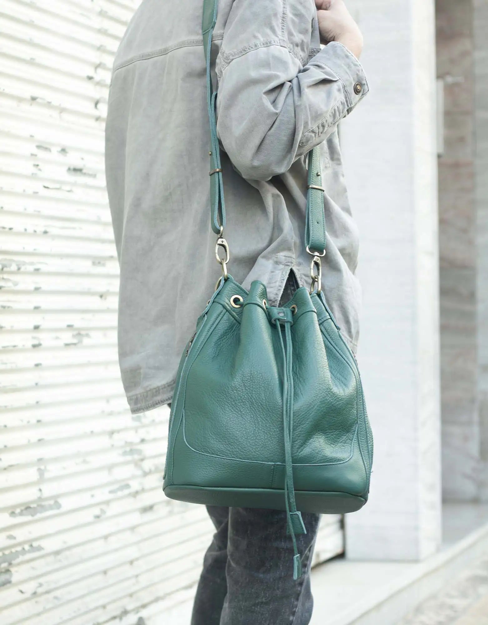 Person holding a green leather bucket bag against a light background