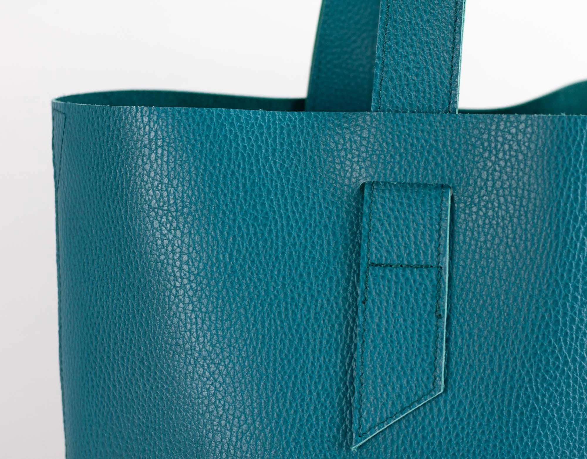 Teal leather tote bag with a pocket on a light gray background