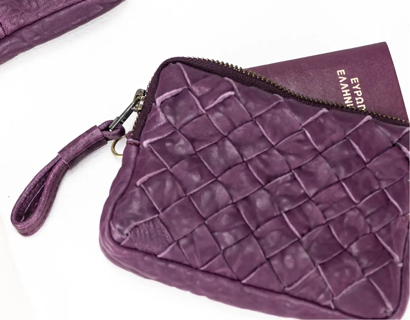 Purple leather crossbody bag with woven pattern and phone on a white background
